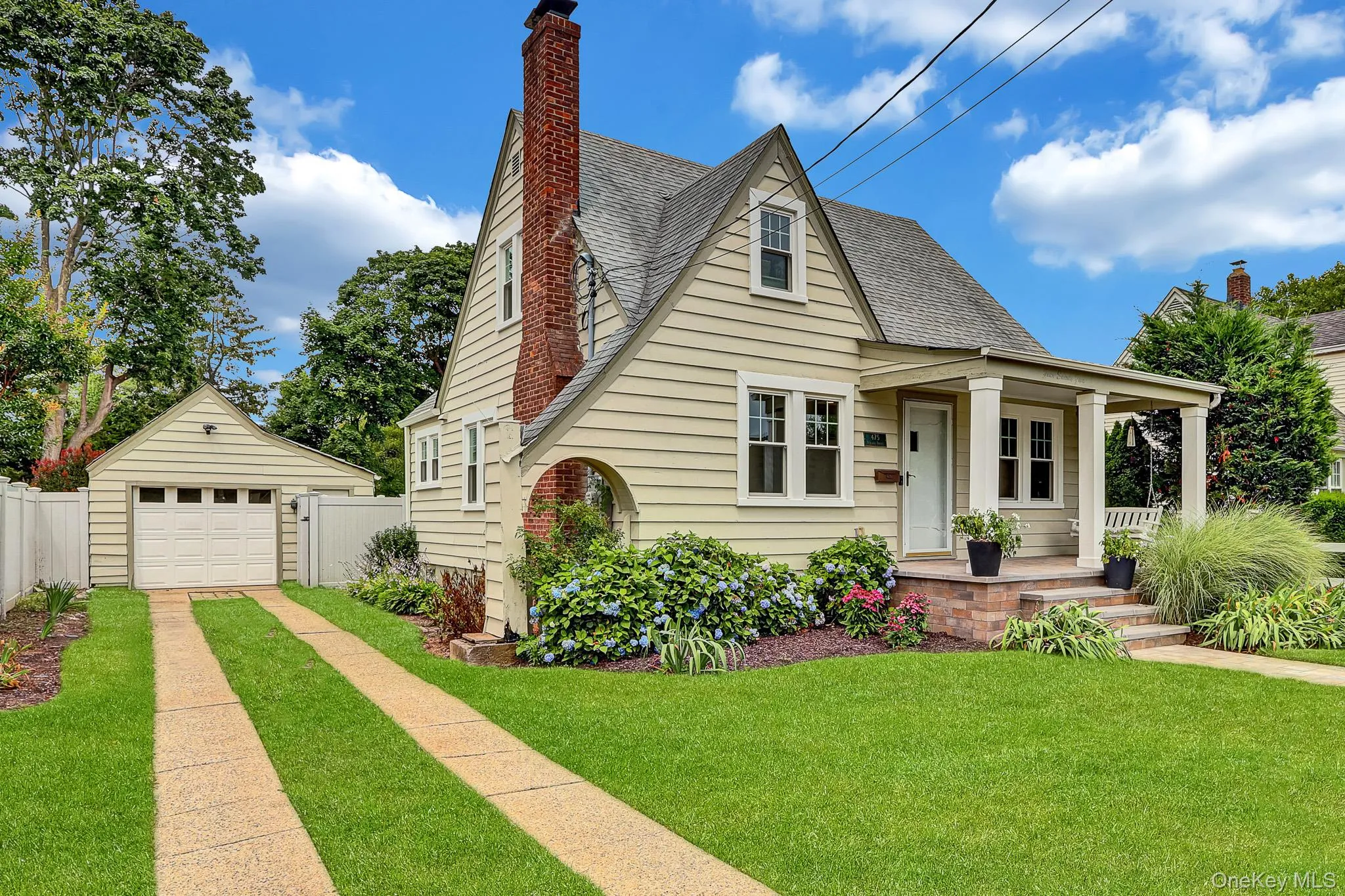 Gable-roofed home with light-colored siding, a prominent brick chimney, and a covered front porch featuring square columns Gable-roofed home with light-colored siding, a prominent brick chimney, and a covered front porch featuring square columns