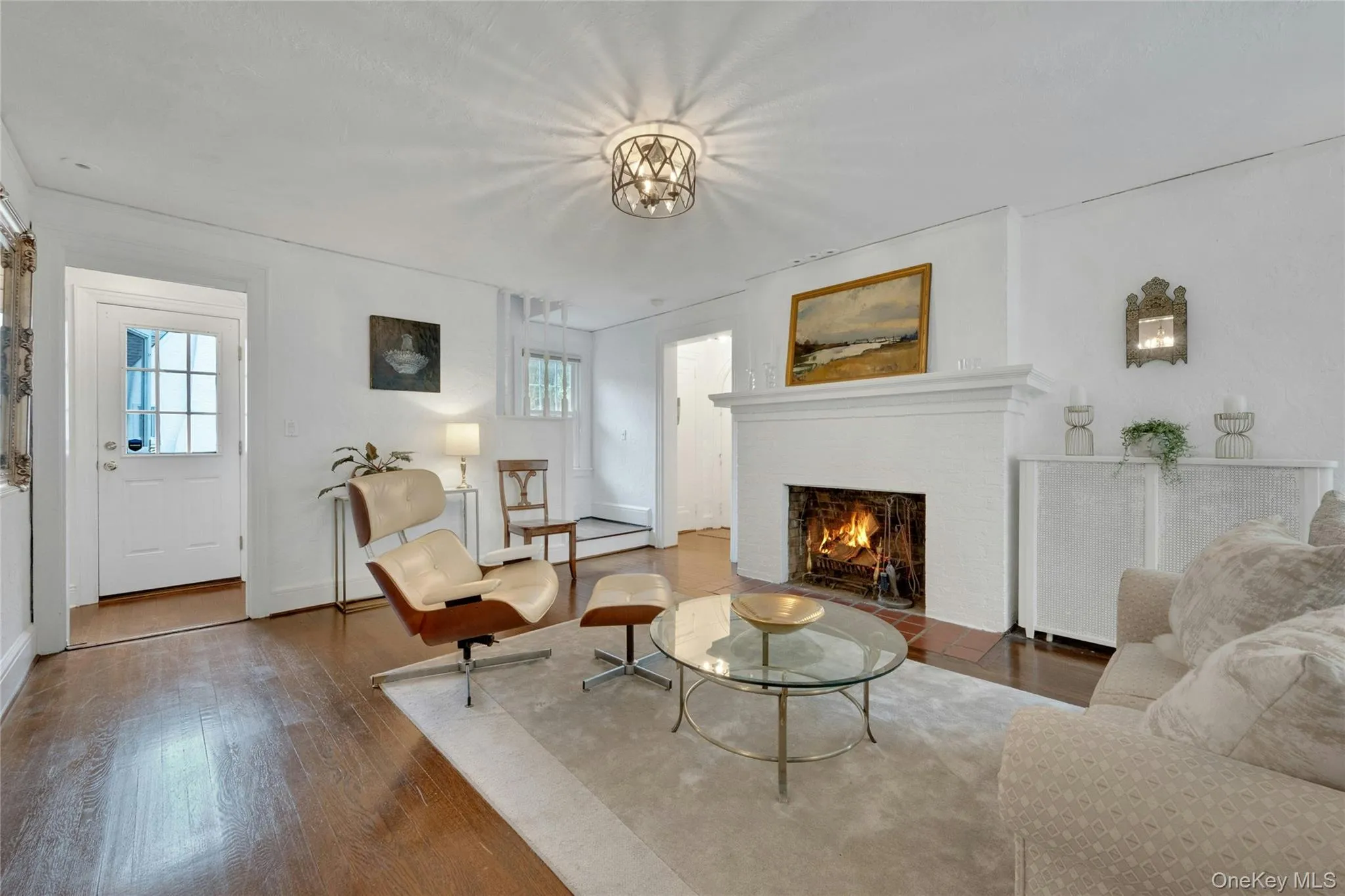 View of the living room with wood burning fireplace and side entry to the house and hallway to the foyer in the background. View of the living room with wood burning fireplace and side entry to the house and hallway to the foyer in the background.