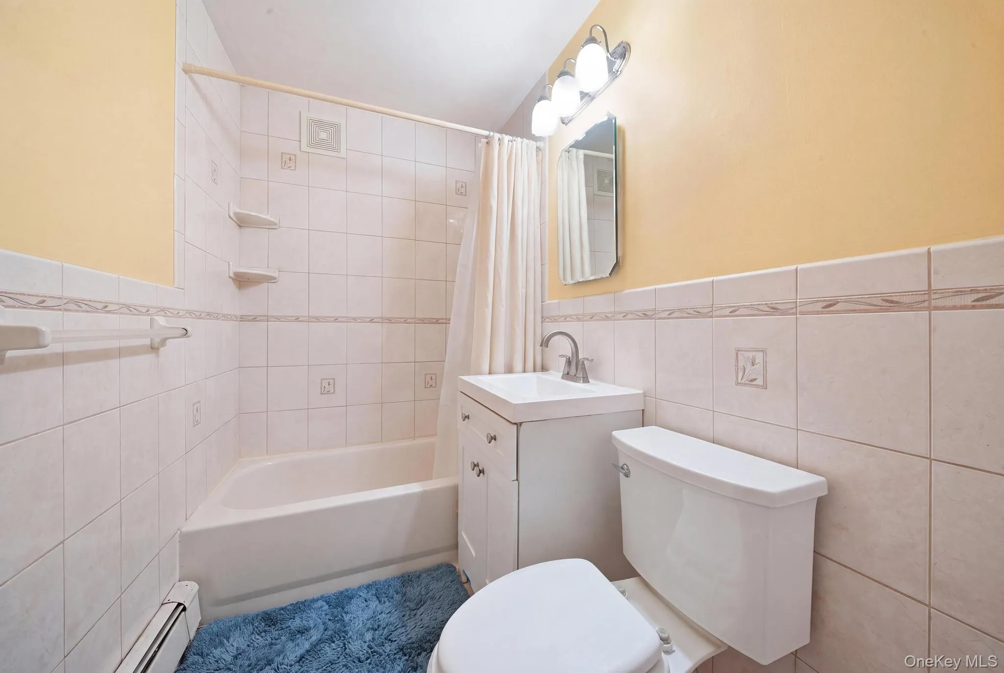 Bathroom featuring a full tub with shower, white tile surround, vanity with sink, and toilet Bathroom featuring a full tub with shower, white tile surround, vanity with sink, and toilet
