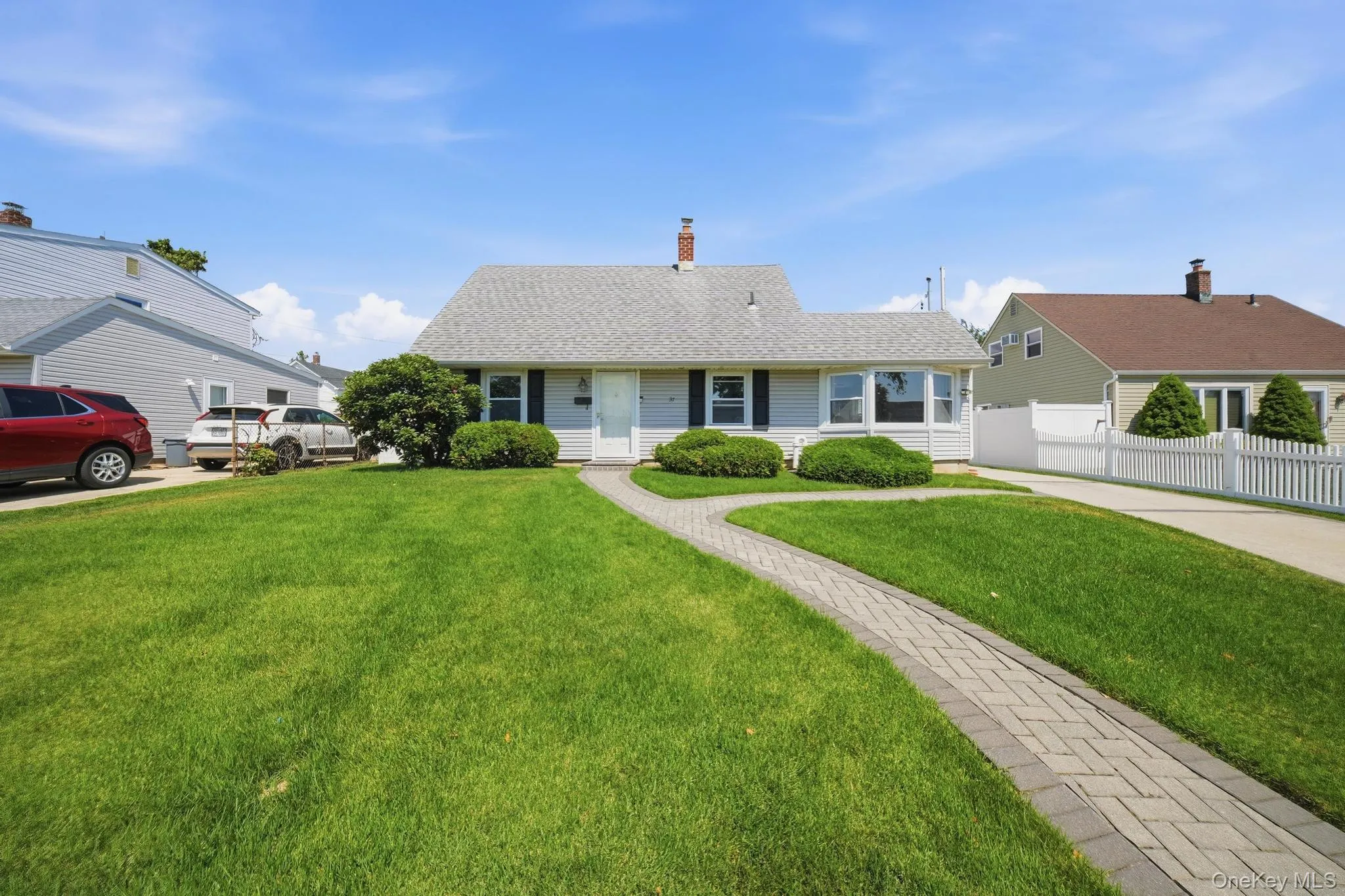 Charming ranch-style residence featuring a light gray exterior, a paved driveway, and a white picket fence Charming ranch-style residence featuring a light gray exterior, a paved driveway, and a white picket fence