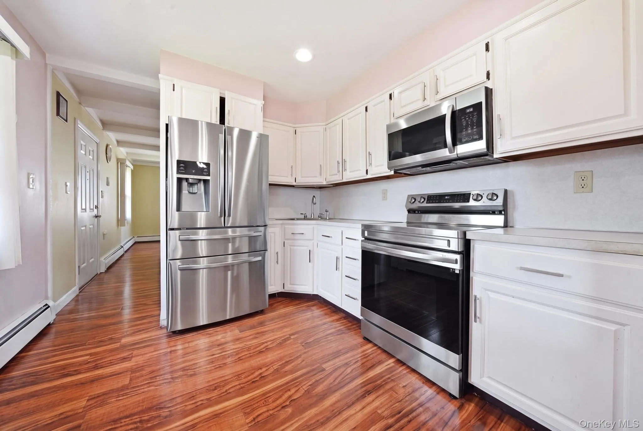Kitchen featuring wood-finish flooring, white cabinetry, stainless steel appliances, and light countertops Kitchen featuring wood-finish flooring, white cabinetry, stainless steel appliances, and light countertops