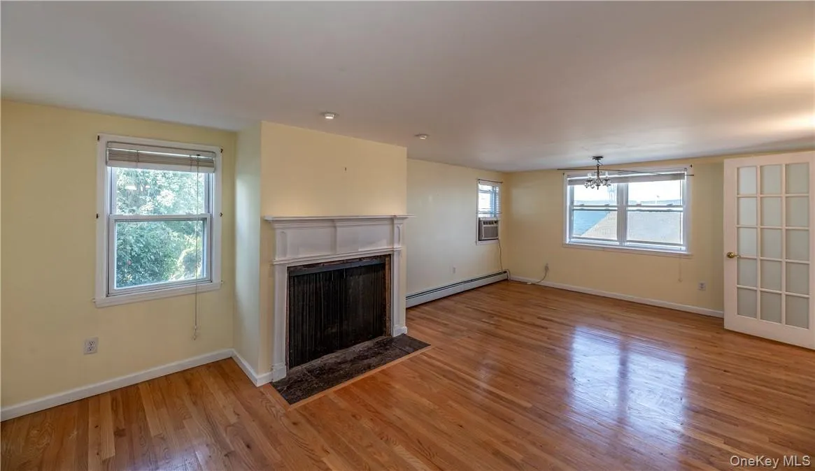 Unfurnished living room featuring a healthy amount of sunlight, hardwood / wood-style flooring, and a baseboard radiator Unfurnished living room featuring a healthy amount of sunlight, hardwood / wood-style flooring, and a baseboard radiator