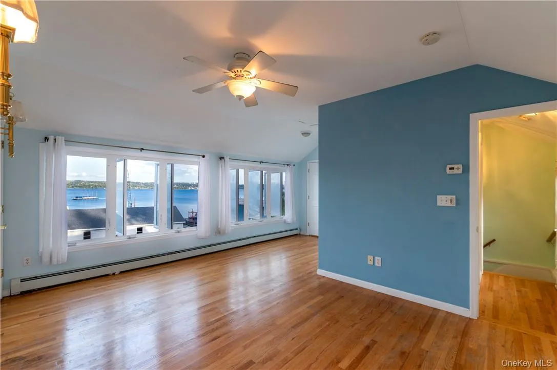 Spare room with a water view, light wood-type flooring, ceiling fan, vaulted ceiling, and baseboard heating Spare room with a water view, light wood-type flooring, ceiling fan, vaulted ceiling, and baseboard heating