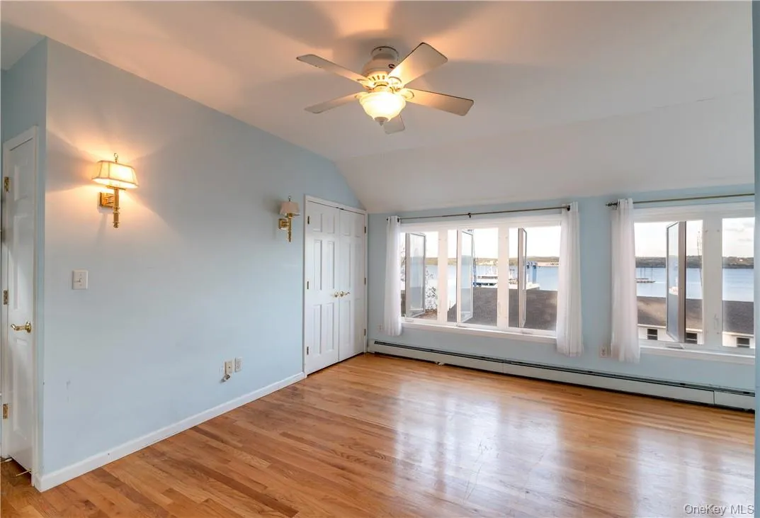 Empty room with a water view, light hardwood / wood-style floors, ceiling fan, vaulted ceiling, and a baseboard heating unit Empty room with a water view, light hardwood / wood-style floors, ceiling fan, vaulted ceiling, and a baseboard heating unit