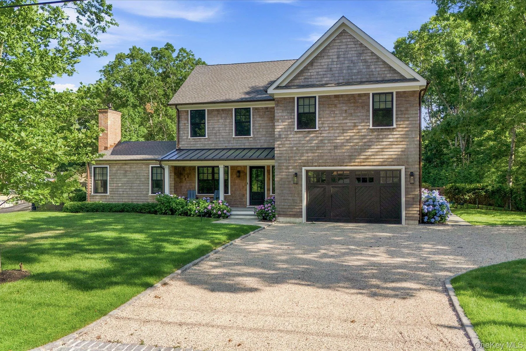 Shingle-style residence featuring a prominent gable, attached two-car garage with carriage-style doors, and a covered front porch Shingle-style residence featuring a prominent gable, attached two-car garage with carriage-style doors, and a covered front porch