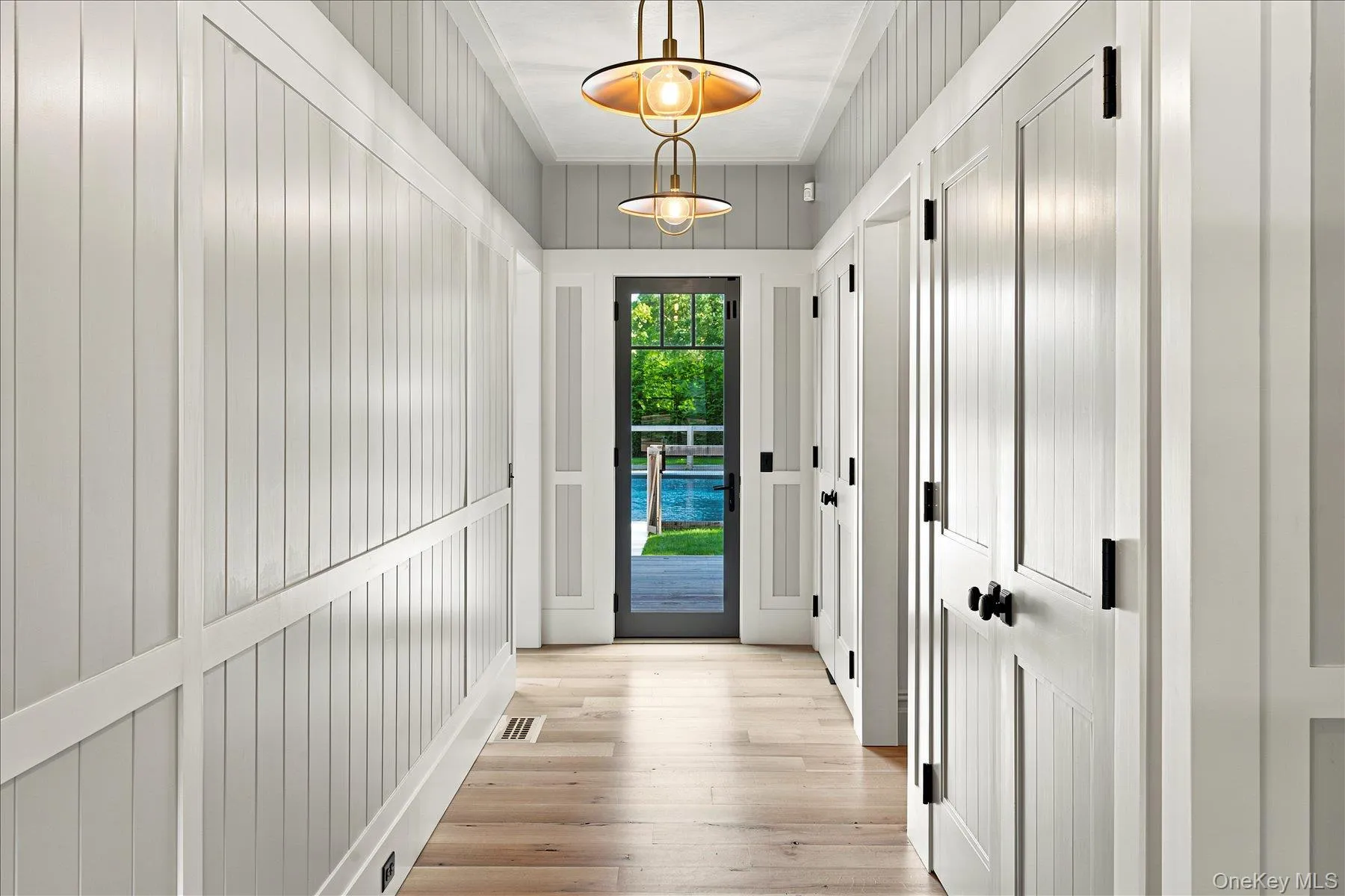 Hallway featuring light wood-finish flooring and vertical paneling walls Hallway featuring light wood-finish flooring and vertical paneling walls