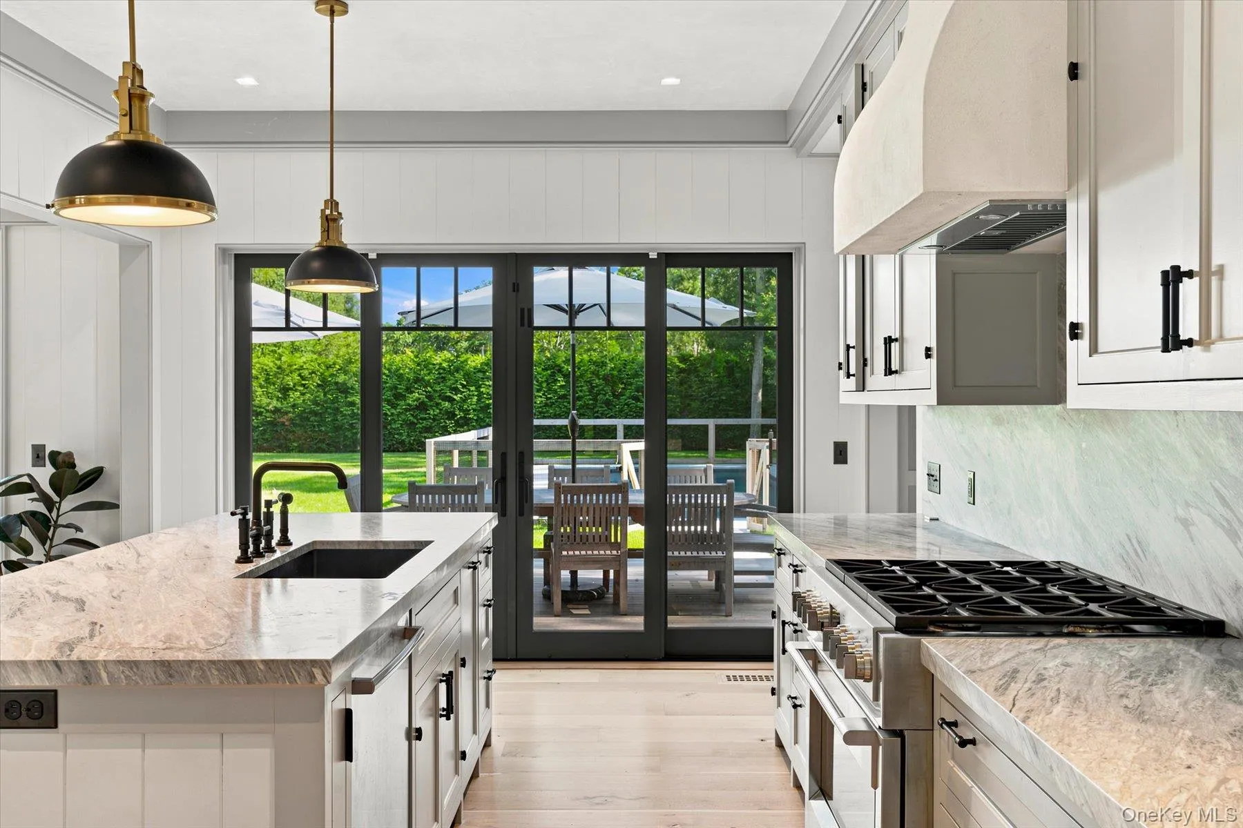 Gourmet kitchen featuring a large center island with integrated sink, stone countertops and backsplash, professional-grade range, and bright wood-finish flooring Gourmet kitchen featuring a large center island with integrated sink, stone countertops and backsplash, professional-grade range, and bright wood-finish flooring