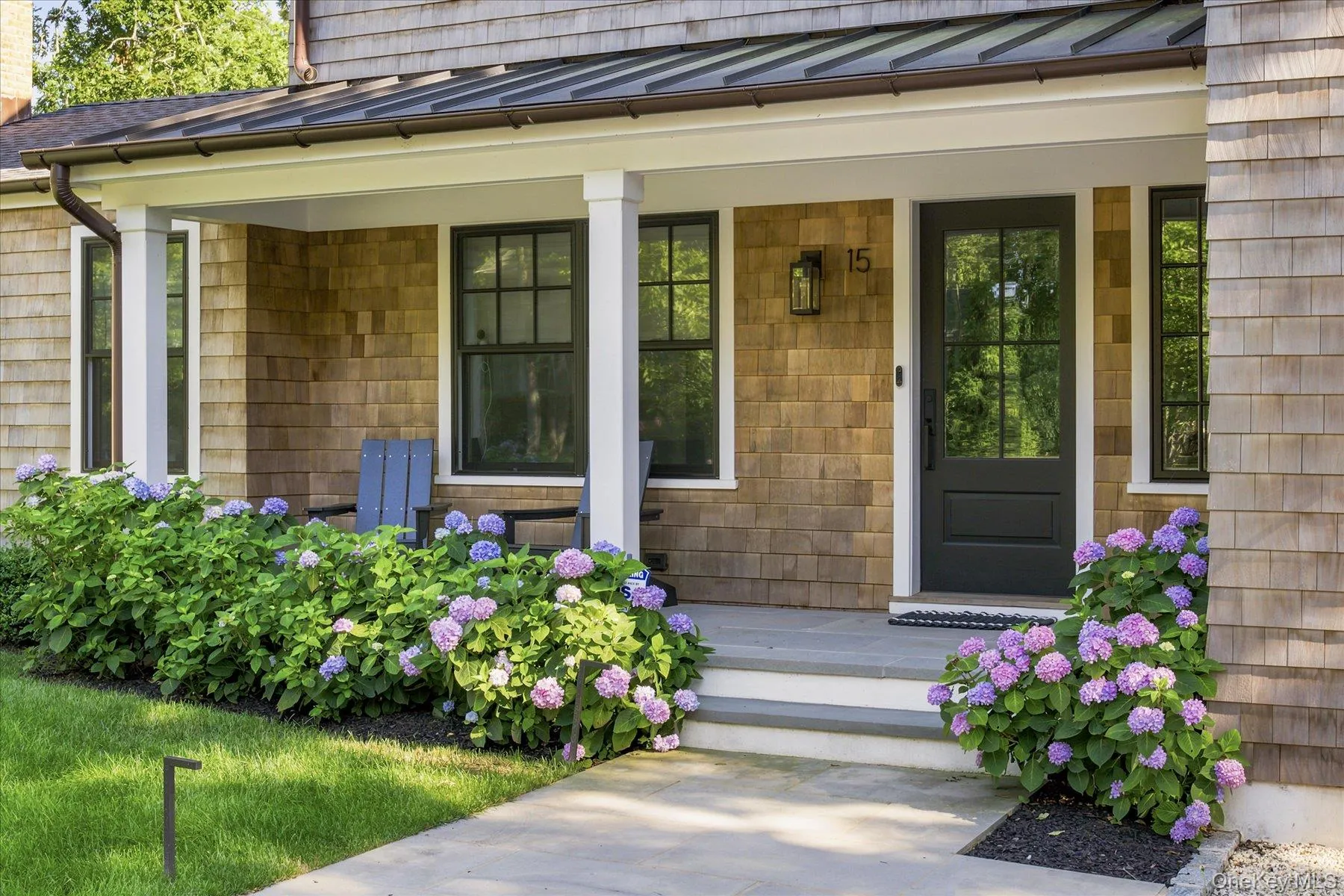 Cedar shingle siding with a covered porch featuring a standing seam roof, white columns, and black-framed windows Cedar shingle siding with a covered porch featuring a standing seam roof, white columns, and black-framed windows