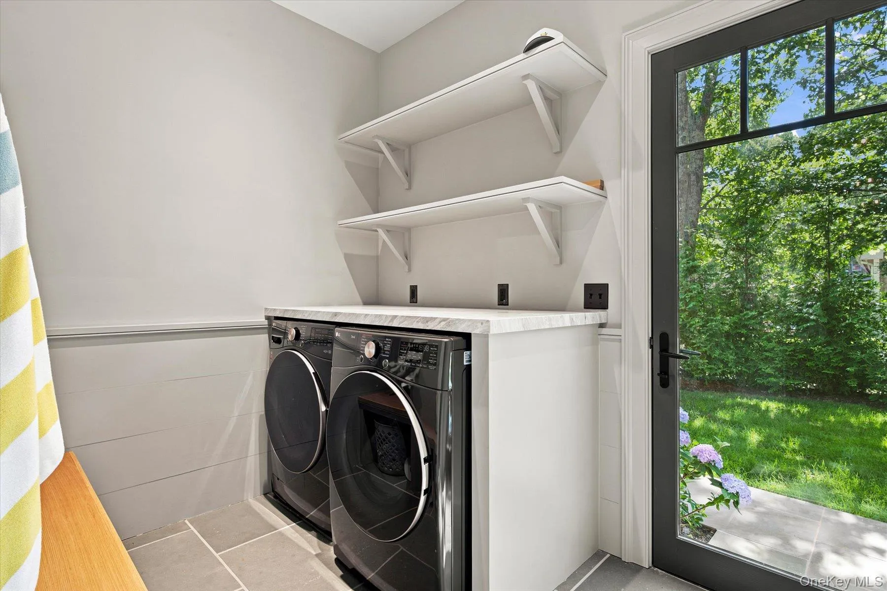Utility room featuring a dark-framed glass paneled door, gray floor tiling, built-in shelving, a full-size washer and dryer, and a counter with a light-colored surface Utility room featuring a dark-framed glass paneled door, gray floor tiling, built-in shelving, a full-size washer and dryer, and a counter with a light-colored surface