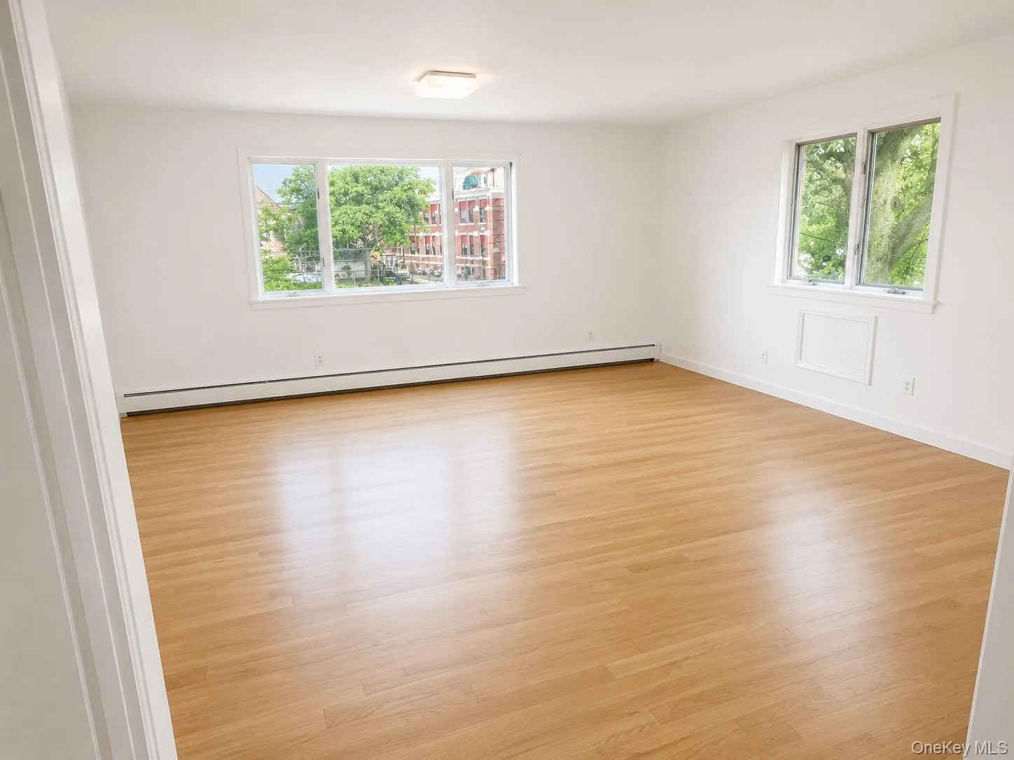 Spacious Living room featuring wood-finish flooring, crisp white walls, and multiple windows Spacious Living room featuring wood-finish flooring, crisp white walls, and multiple windows