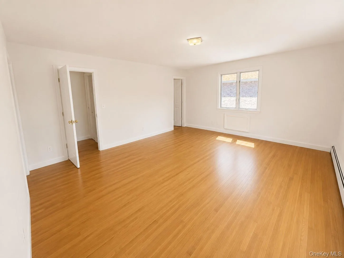 Spacious interior featuring wood-finish flooring, white walls, and a ceiling-mounted light fixture Spacious interior featuring wood-finish flooring, white walls, and a ceiling-mounted light fixture