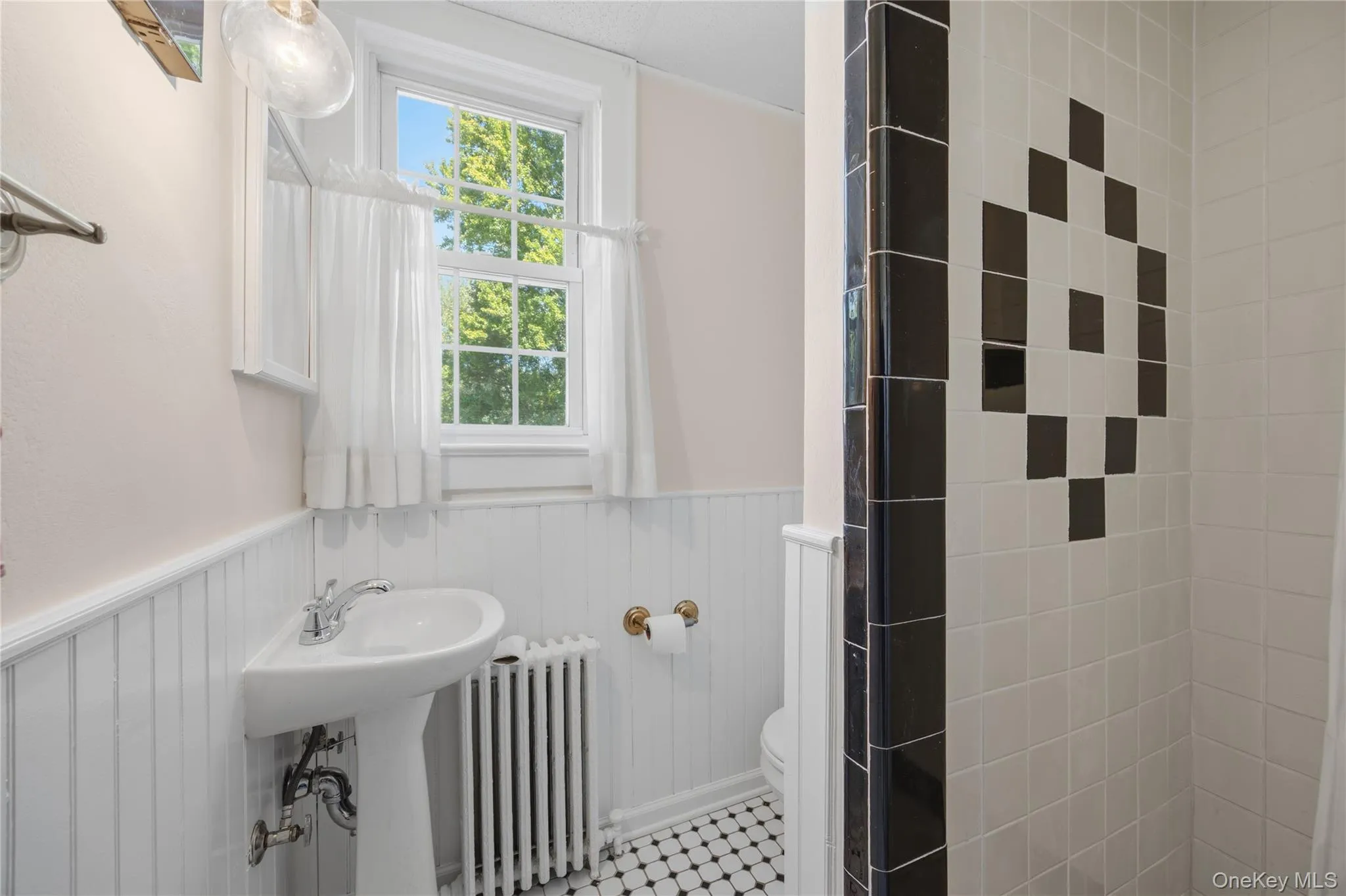 Main floor full bathroom with a tiled walk-in shower, wainscoting and a pedestal sink Main floor full bathroom with a tiled walk-in shower, wainscoting and a pedestal sink
