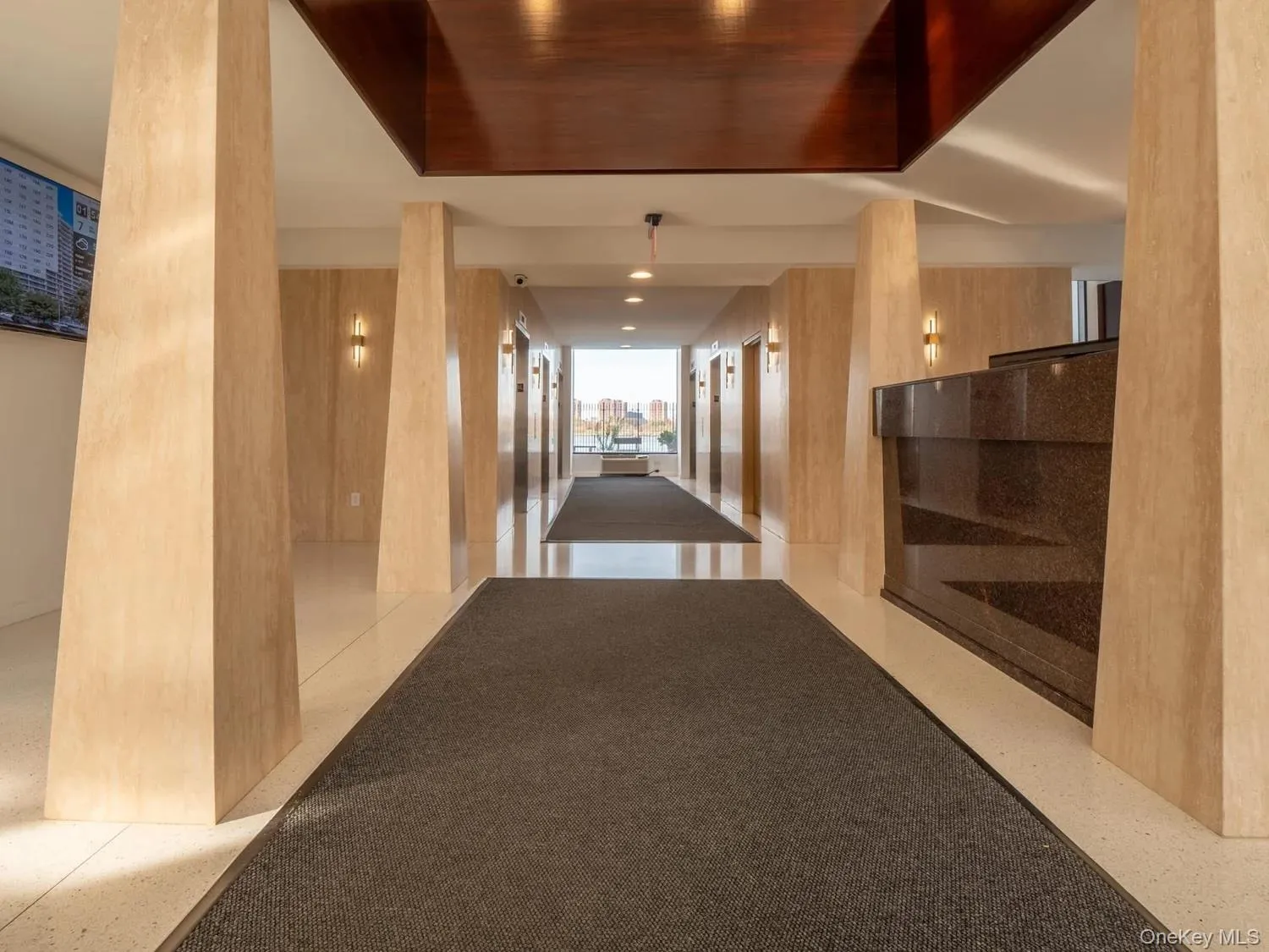 Lobby entry featuring stone-clad columns, polished flooring, a dark stone reception desk, and recessed lighting Lobby entry featuring stone-clad columns, polished flooring, a dark stone reception desk, and recessed lighting