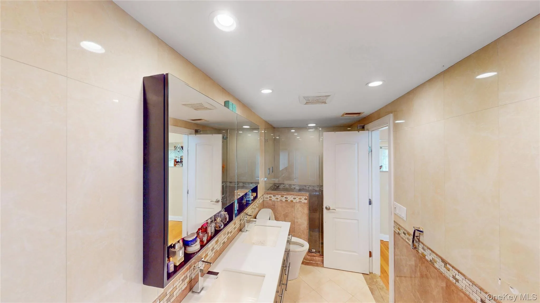 Bathroom featuring full-height tiled walls, recessed lighting, a dual vanity with undermount sinks, and a built-in mirrored cabinet Bathroom featuring full-height tiled walls, recessed lighting, a dual vanity with undermount sinks, and a built-in mirrored cabinet