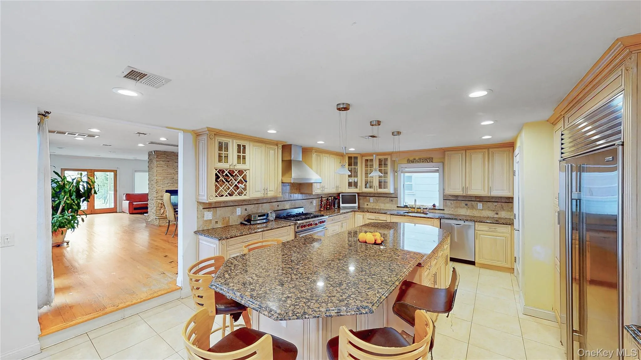 Spacious kitchen featuring an expansive island with a stone countertop, light wood-finish cabinetry, stainless steel appliances, and recessed lighting Spacious kitchen featuring an expansive island with a stone countertop, light wood-finish cabinetry, stainless steel appliances, and recessed lighting