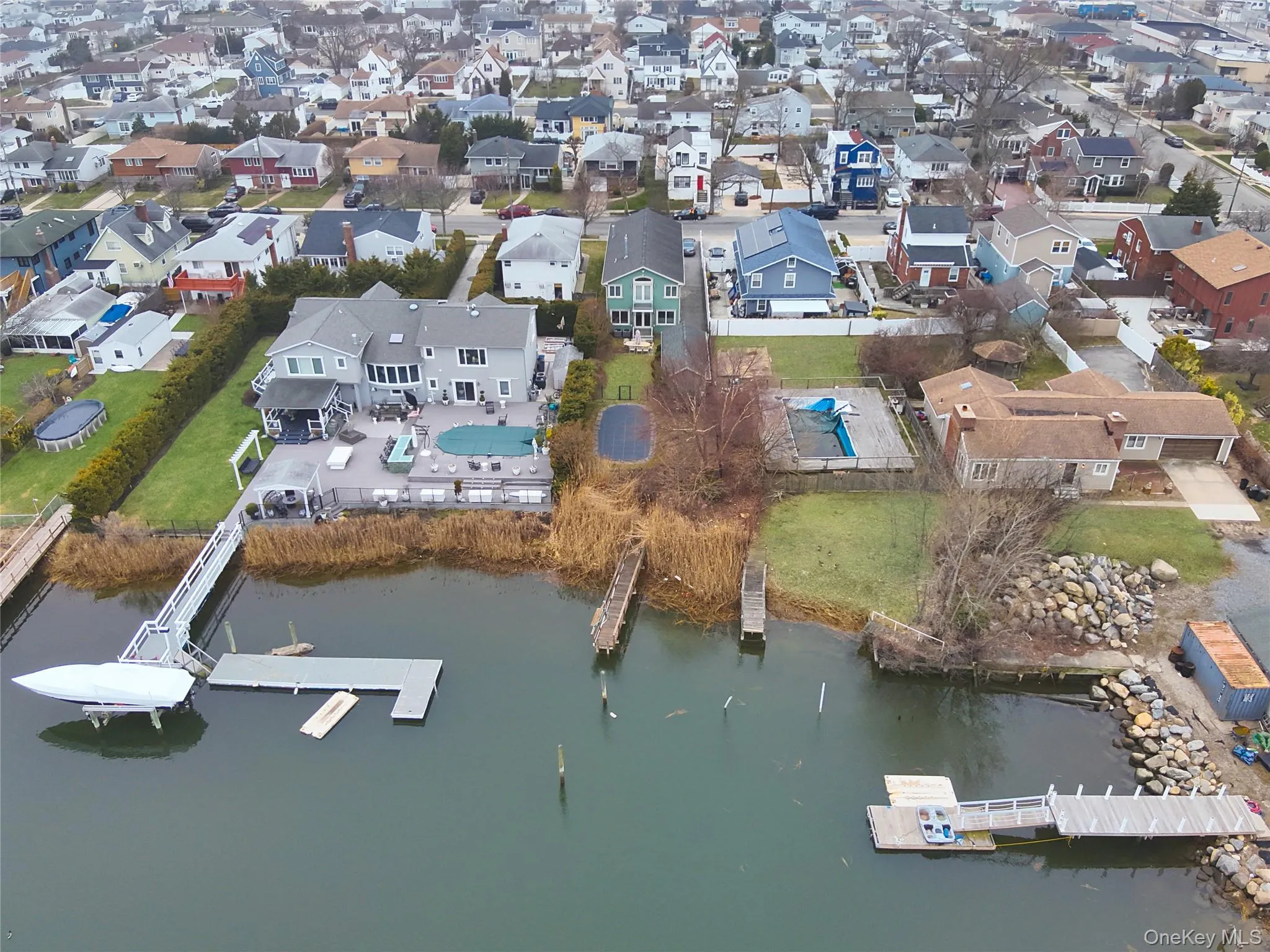 Waterfront property featuring a private boat dock, extensive rear decking, an in-ground swimming pool, and a manicured lawn Waterfront property featuring a private boat dock, extensive rear decking, an in-ground swimming pool, and a manicured lawn