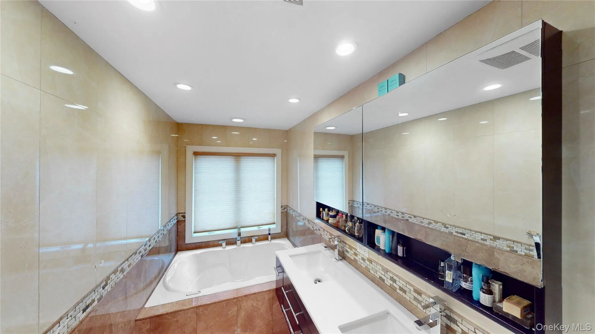 Bathroom featuring a built-in tub, dual sink vanity with chrome fixtures, and a large wall-mounted mirror Bathroom featuring a built-in tub, dual sink vanity with chrome fixtures, and a large wall-mounted mirror
