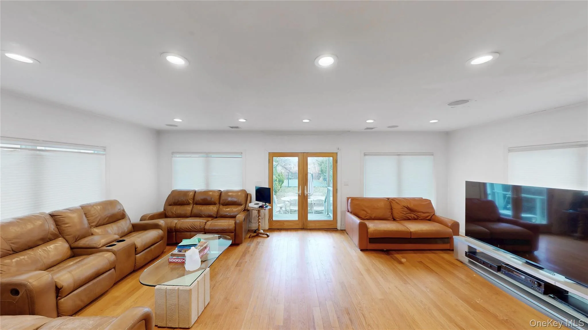 Spacious living area featuring light wood-finish flooring, recessed lighting, and multiple windows with blinds Spacious living area featuring light wood-finish flooring, recessed lighting, and multiple windows with blinds