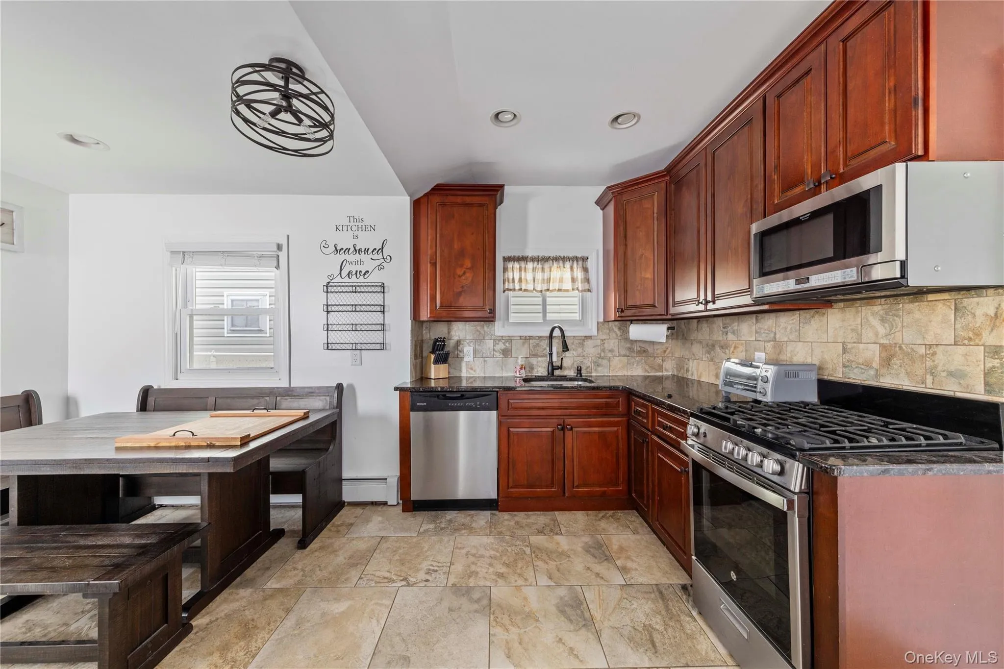 Kitchen featuring wood cabinetry, stainless steel appliances, dark countertops, and tile backsplash Kitchen featuring wood cabinetry, stainless steel appliances, dark countertops, and tile backsplash