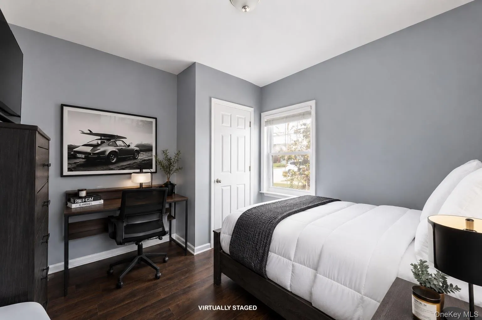 Bedroom featuring wood-finish flooring look, light grey painted walls, a white paneled door, and a single window with white trim. Bedroom featuring wood-finish flooring look, light grey painted walls, a white paneled door, and a single window with white trim.