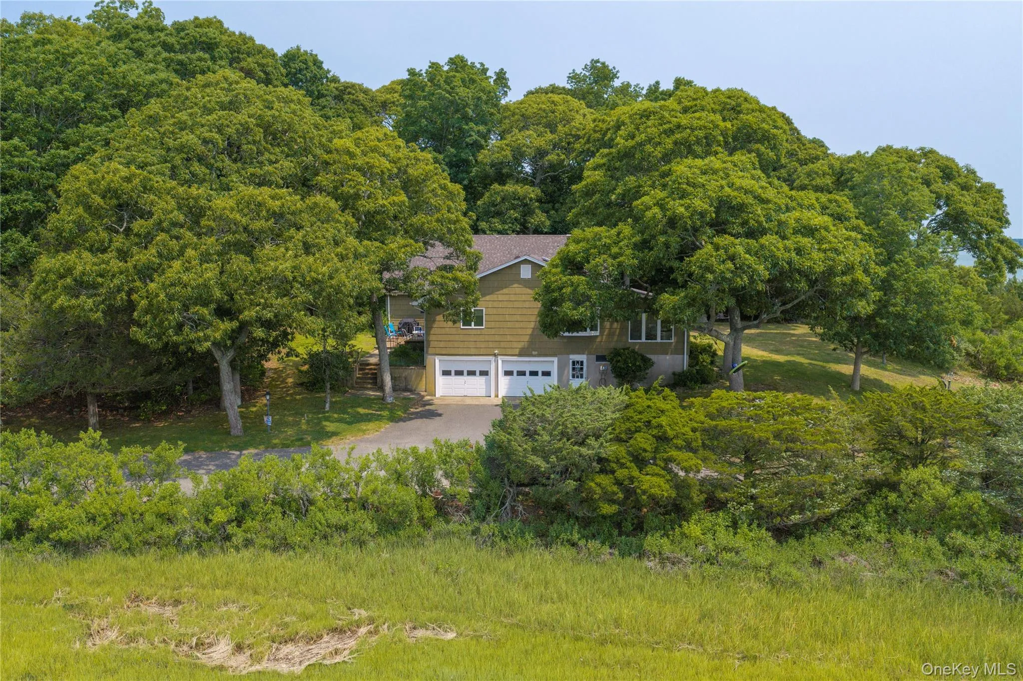 Split-level residence featuring a two-car garage with white doors, surrounded by abundant mature trees and natural landscaping Split-level residence featuring a two-car garage with white doors, surrounded by abundant mature trees and natural landscaping