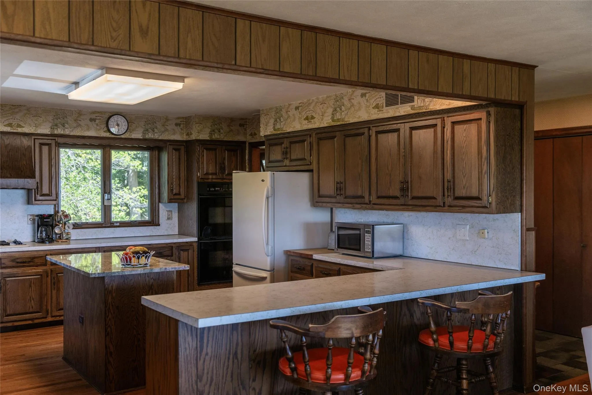 Kitchen featuring wood-finish cabinetry, a central island with countertop, and an integrated breakfast bar Kitchen featuring wood-finish cabinetry, a central island with countertop, and an integrated breakfast bar
