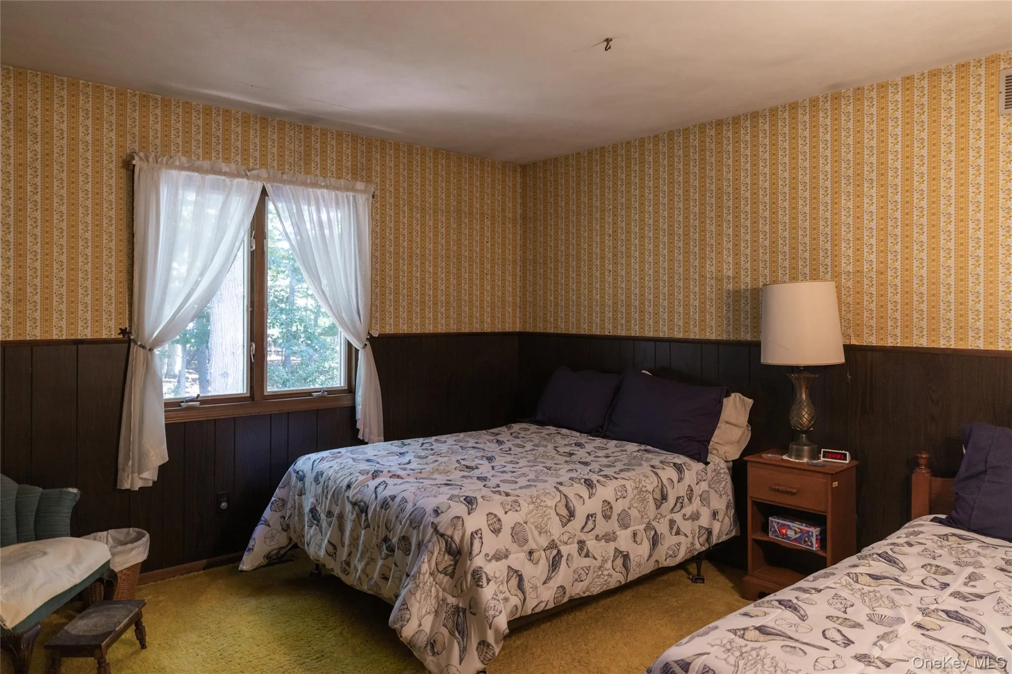 Room featuring a window with white sheer curtains that gently blow with the bay breezes dark wood paneling, patterned wallpaper, and carpet flooring Room featuring a window with white sheer curtains that gently blow with the bay breezes dark wood paneling, patterned wallpaper, and carpet flooring