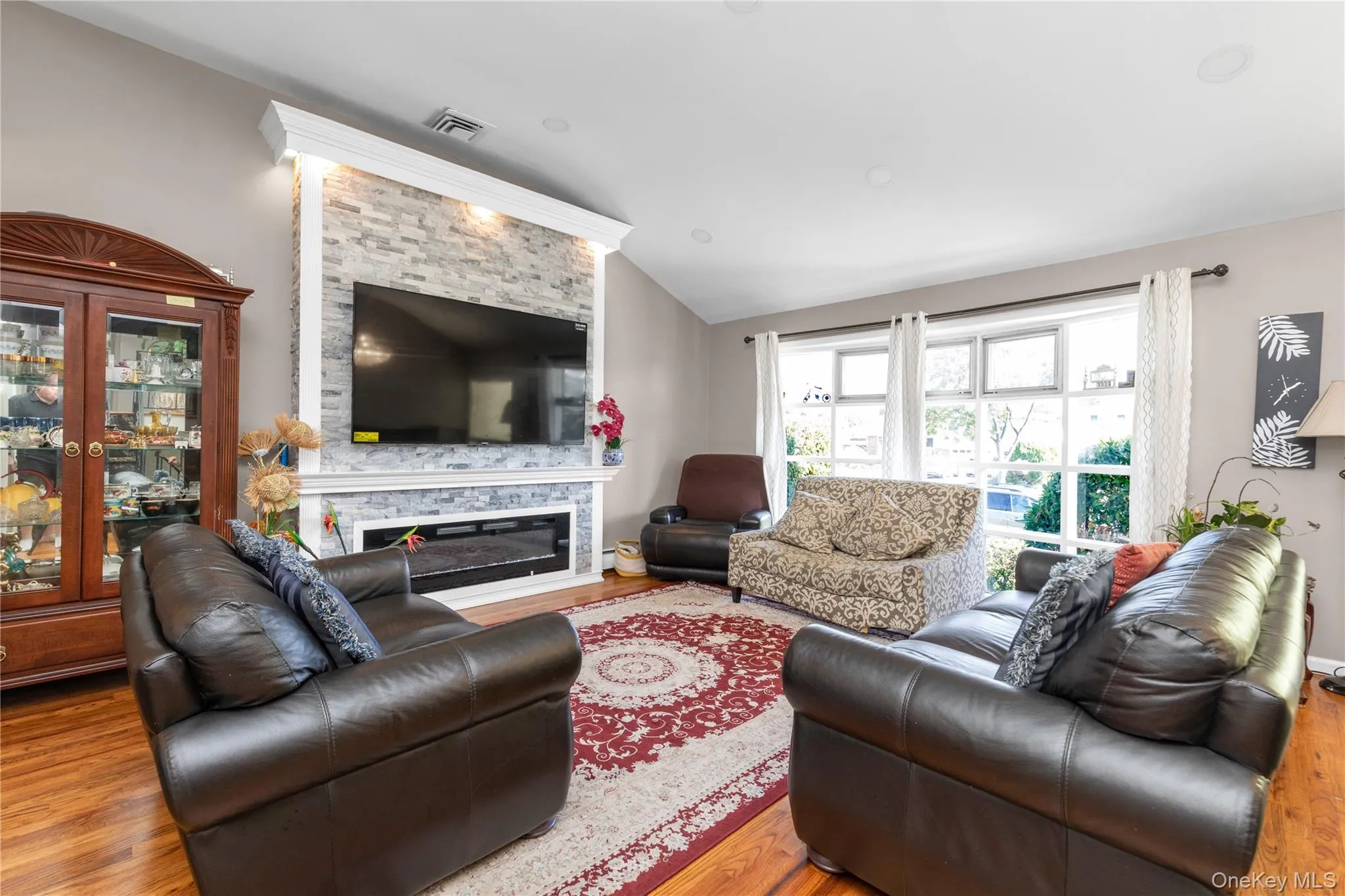 Living room featuring lofted ceiling, wood finished floors, and a stone fireplace Living room featuring lofted ceiling, wood finished floors, and a stone fireplace