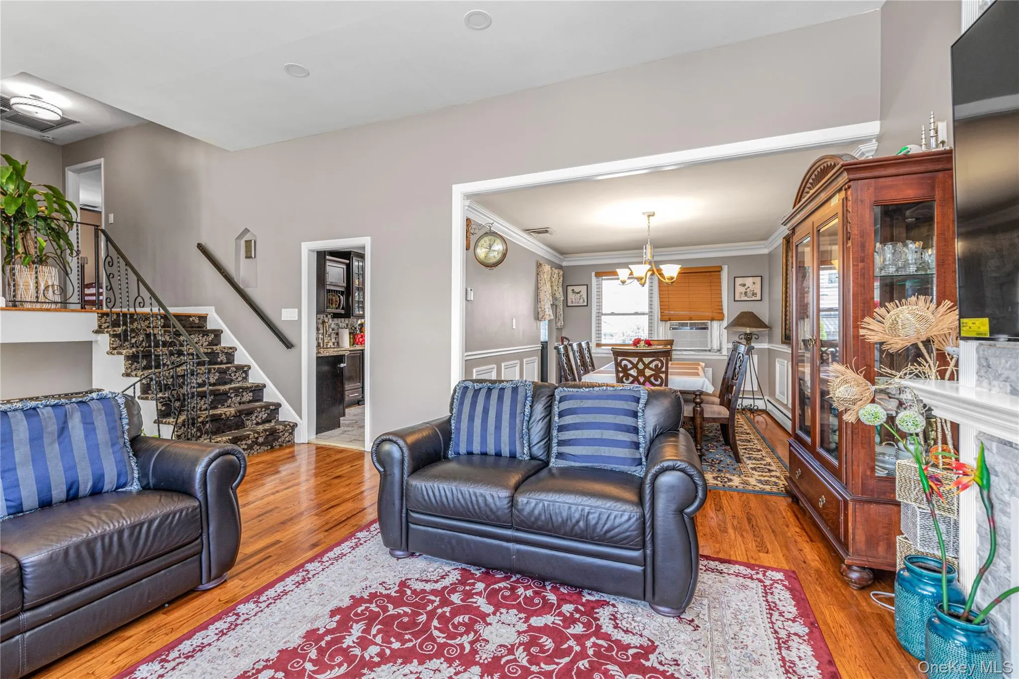 Living room with wood finished floors, stairway, a chandelier, and ornamental molding Living room with wood finished floors, stairway, a chandelier, and ornamental molding