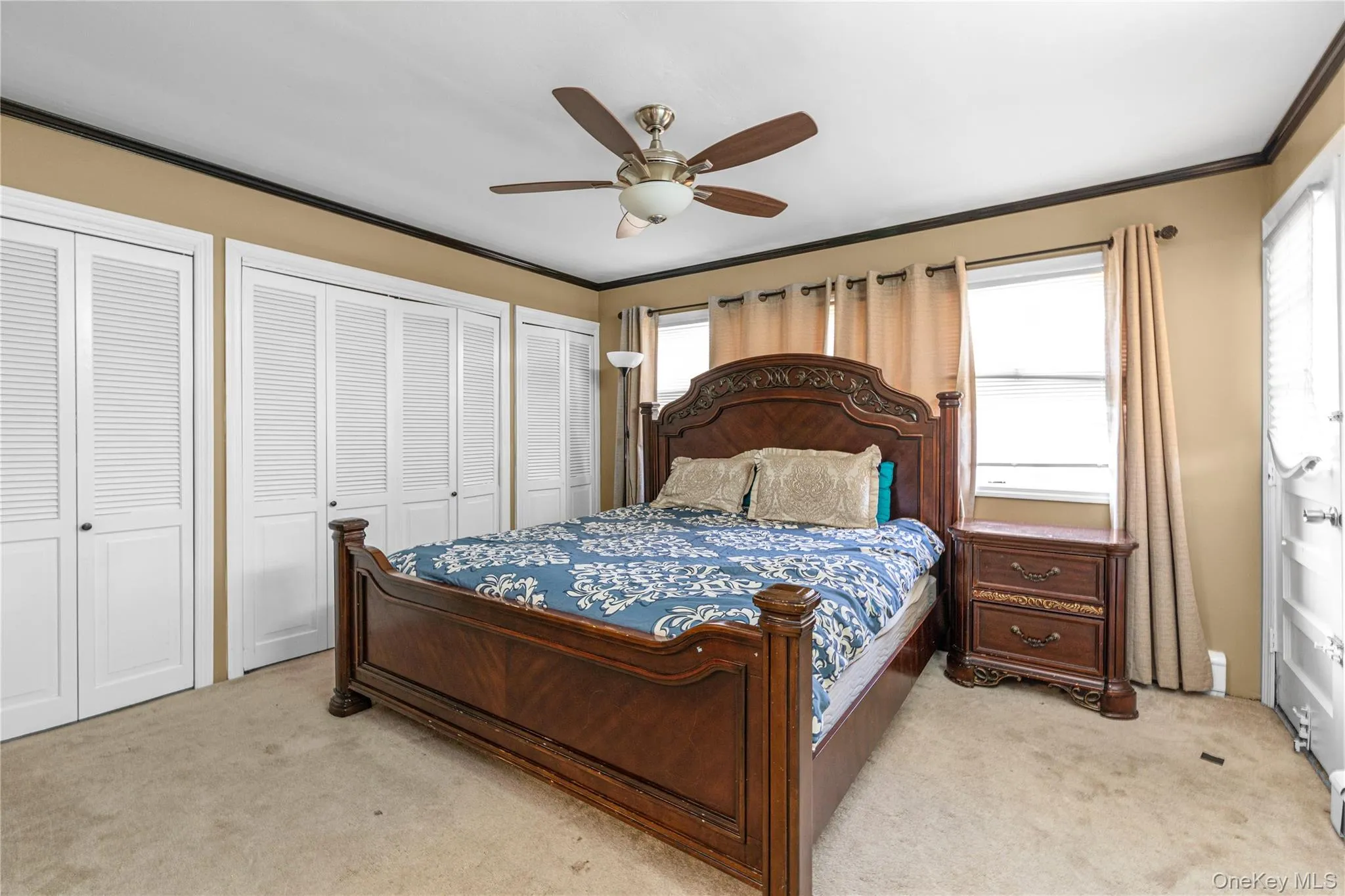 Bedroom with multiple closets, crown molding, light colored carpet, and ceiling fan Bedroom with multiple closets, crown molding, light colored carpet, and ceiling fan