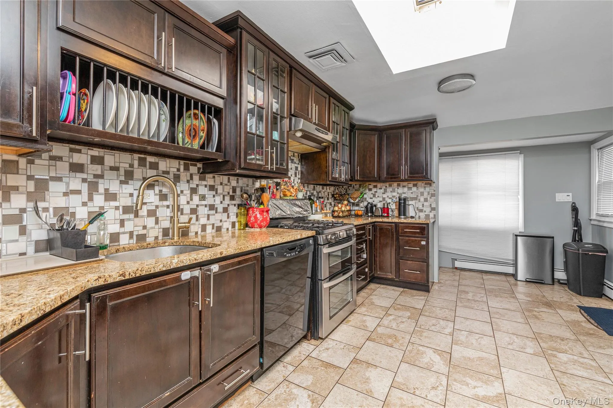 Kitchen featuring dark brown cabinetry, glass insert cabinets, light stone counters, tasteful backsplash, and range with two ovens Kitchen featuring dark brown cabinetry, glass insert cabinets, light stone counters, tasteful backsplash, and range with two ovens