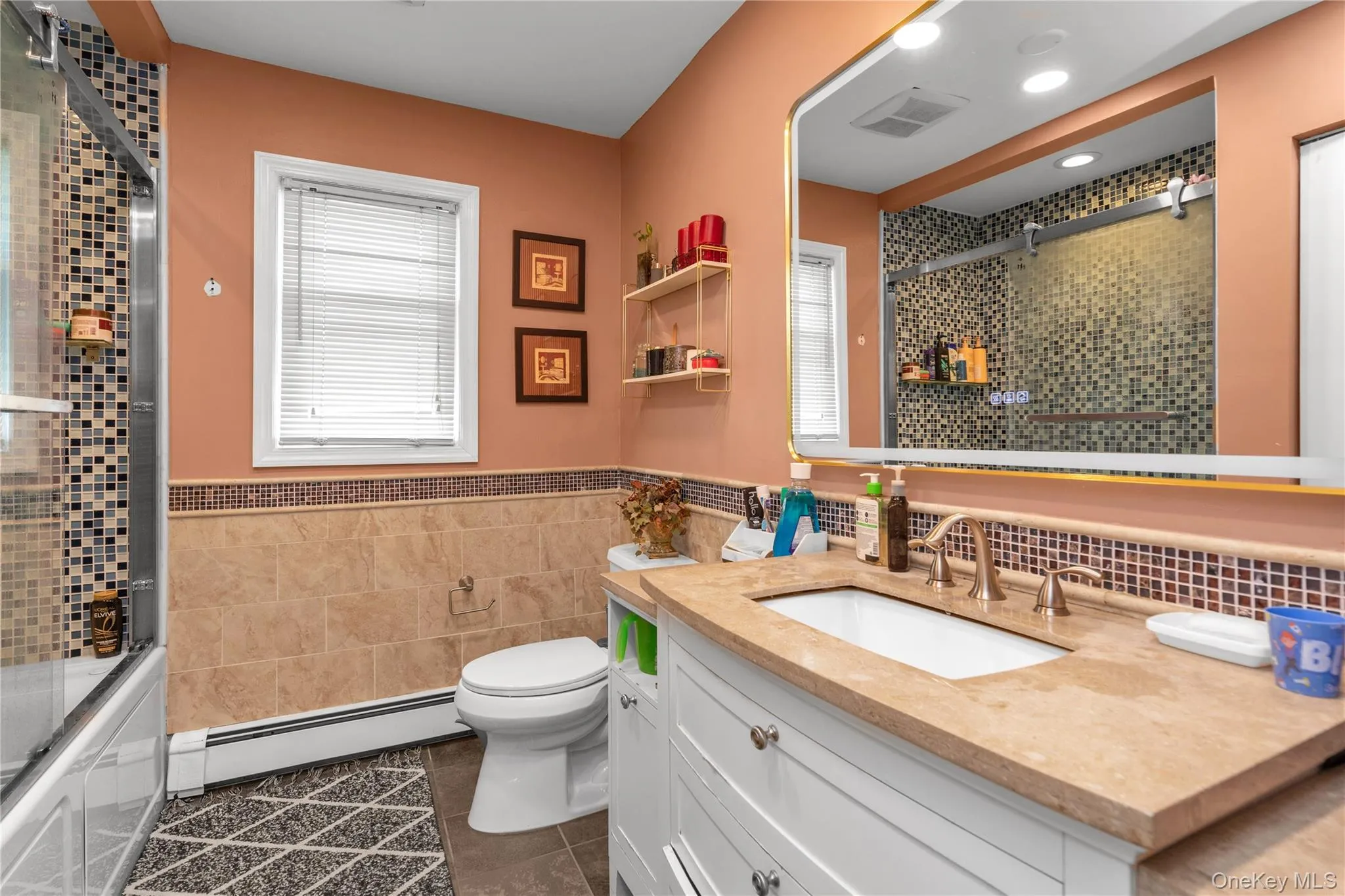 Full bathroom featuring dark tile patterned flooring, tile walls, vanity, a baseboard heating unit, and enclosed tub / shower combo Full bathroom featuring dark tile patterned flooring, tile walls, vanity, a baseboard heating unit, and enclosed tub / shower combo