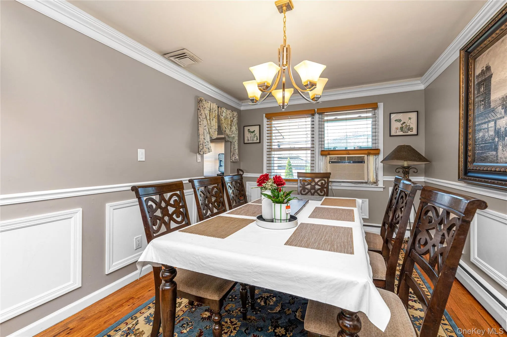Dining space with crown molding, wainscoting, a chandelier, wood finished floors, and a baseboard radiator Dining space with crown molding, wainscoting, a chandelier, wood finished floors, and a baseboard radiator