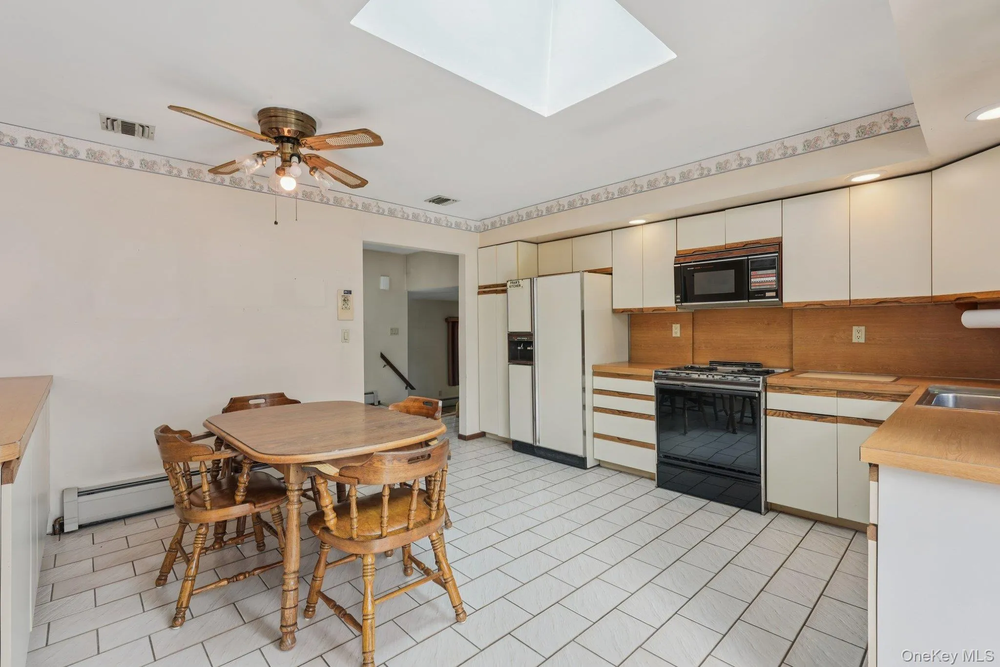 Kitchen featuring black appliances, light countertops, a skylight, and white cabinets Kitchen featuring black appliances, light countertops, a skylight, and white cabinets