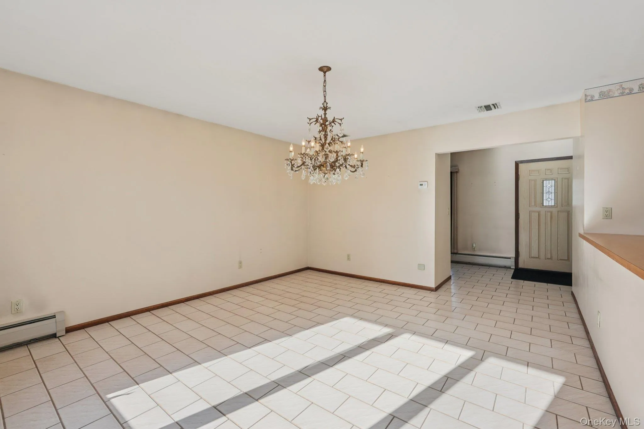 Unfurnished room with light tile patterned floors, a chandelier, and a baseboard heating unit Unfurnished room with light tile patterned floors, a chandelier, and a baseboard heating unit