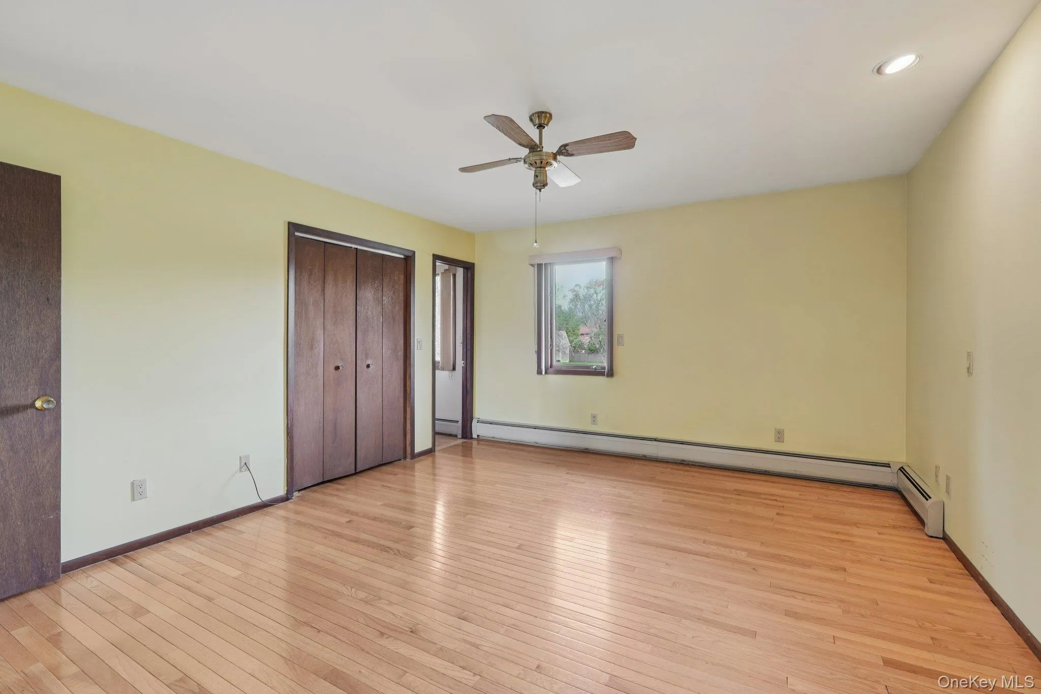 Unfurnished bedroom featuring light wood-style flooring, two closets, a ceiling fan, and baseboard heating Unfurnished bedroom featuring light wood-style flooring, two closets, a ceiling fan, and baseboard heating