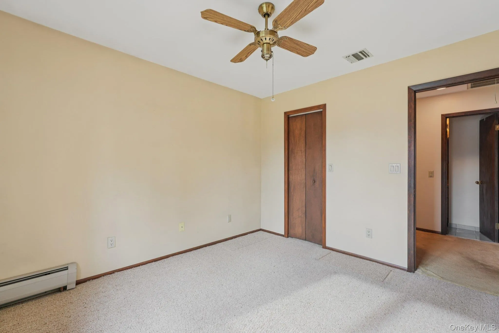 Unfurnished bedroom with carpet, baseboard heating, a ceiling fan, and a closet Unfurnished bedroom with carpet, baseboard heating, a ceiling fan, and a closet