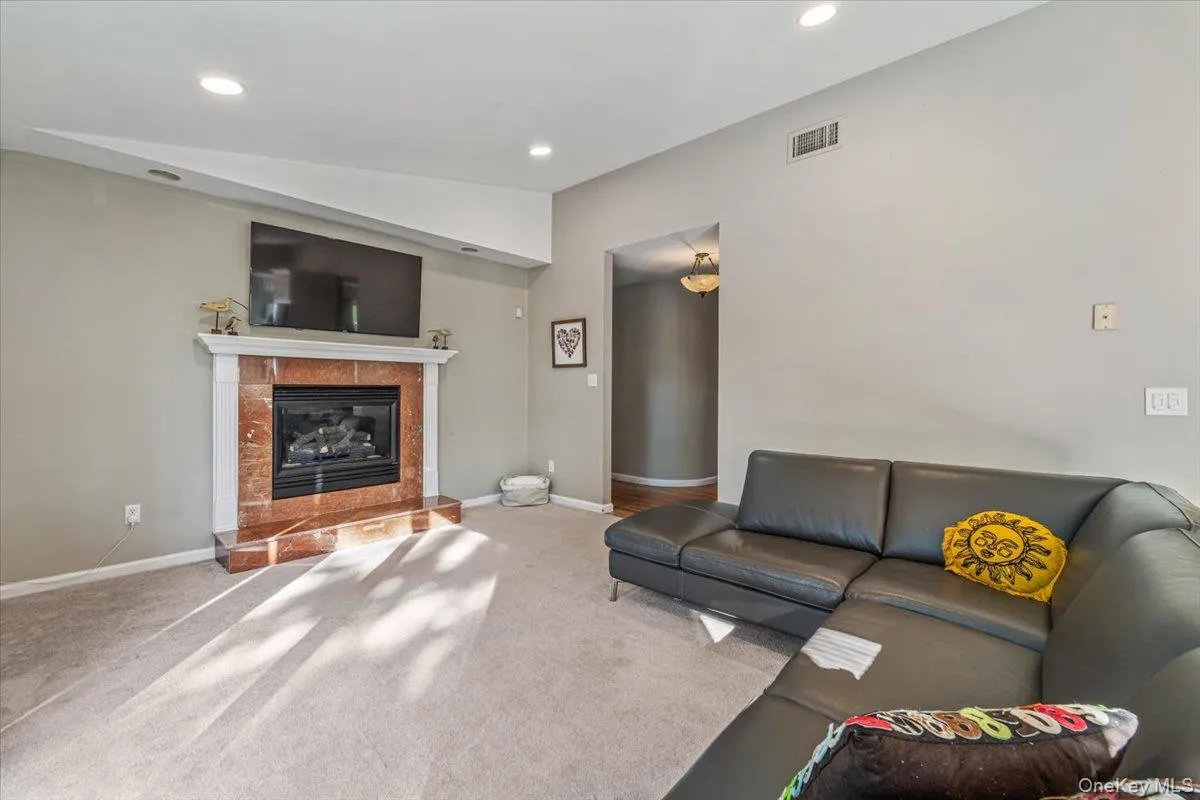 Living area featuring a fireplace with a stone-finish surround and white mantel, recessed lighting, carpet flooring, and a wall-mounted television Living area featuring a fireplace with a stone-finish surround and white mantel, recessed lighting, carpet flooring, and a wall-mounted television