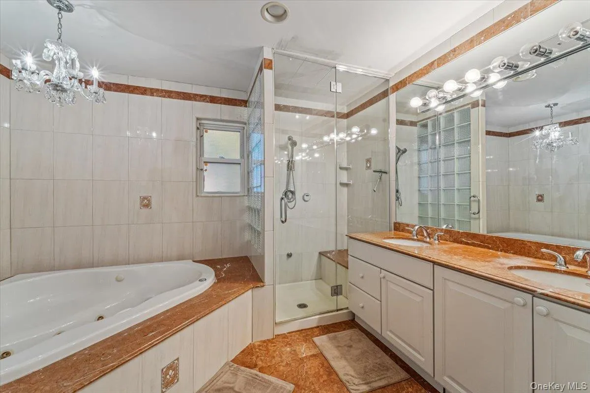 Bathroom featuring a built-in jetted tub, a glass-enclosed shower with a bench, and a dual-sink vanity with white cabinetry Bathroom featuring a built-in jetted tub, a glass-enclosed shower with a bench, and a dual-sink vanity with white cabinetry