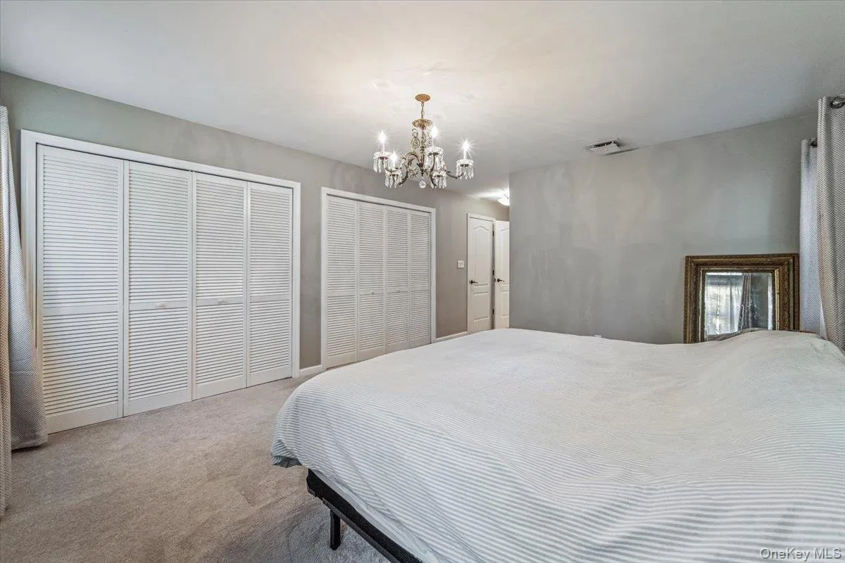 Spacious room featuring light gray walls, plush carpeting, a chandelier-style ceiling light, and multiple louvered bifold closet doors Spacious room featuring light gray walls, plush carpeting, a chandelier-style ceiling light, and multiple louvered bifold closet doors