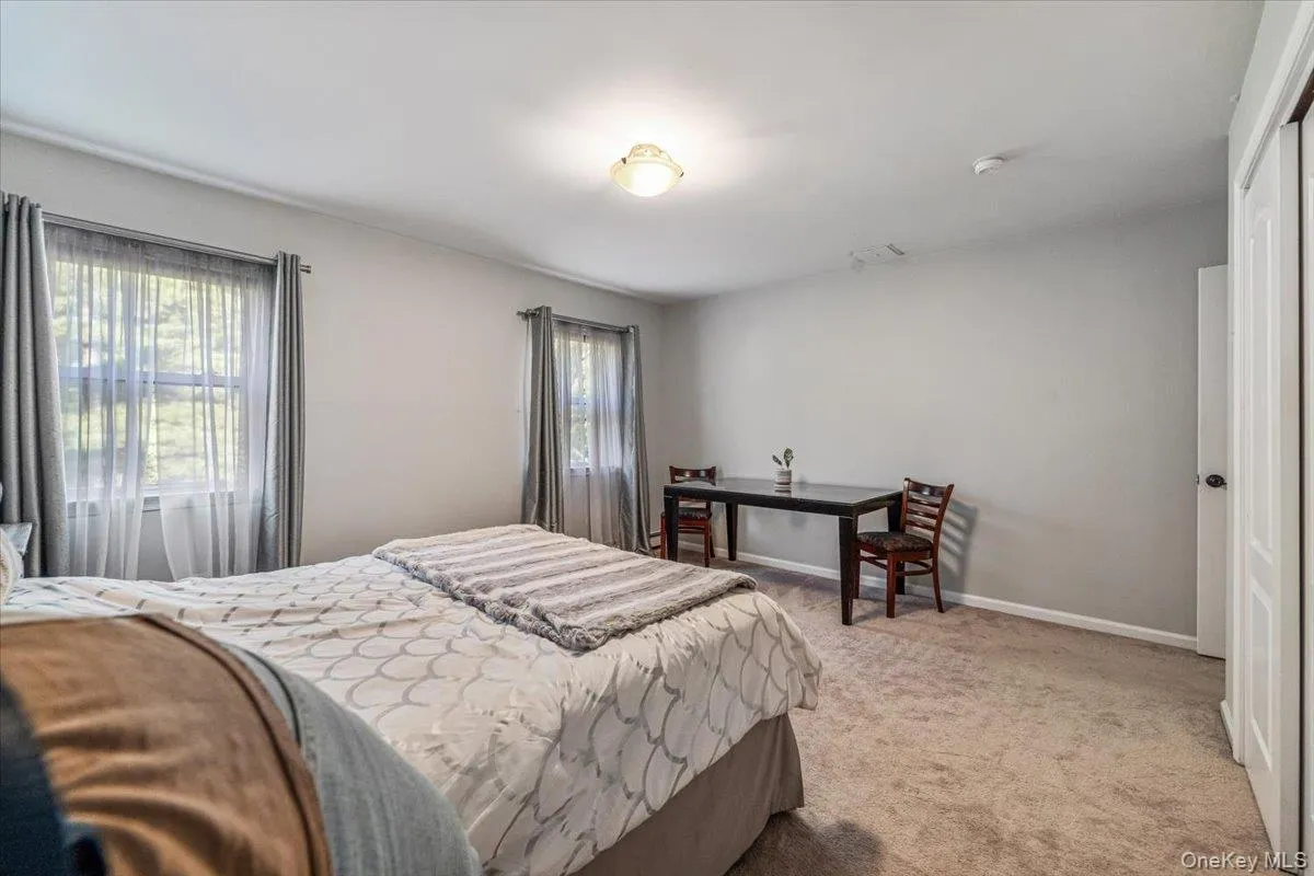 Carpeted room featuring multiple windows with sheer and opaque curtains, a ceiling-mounted light fixture, and a white panel door Carpeted room featuring multiple windows with sheer and opaque curtains, a ceiling-mounted light fixture, and a white panel door