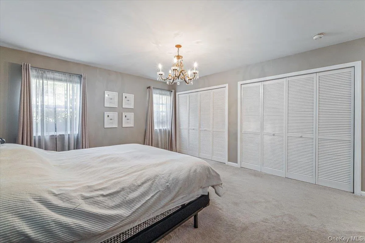 Carpeted room featuring a chandelier, two windows with draperies, and multiple louvered bi-fold closet doors Carpeted room featuring a chandelier, two windows with draperies, and multiple louvered bi-fold closet doors