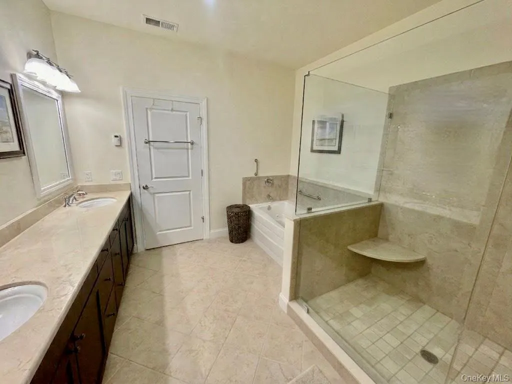 Bathroom featuring a dual vanity with undermount sinks, a built-in soaking tub, a glass-enclosed shower with a built-in corner shelf, tile flooring, and a paneled door Bathroom featuring a dual vanity with undermount sinks, a built-in soaking tub, a glass-enclosed shower with a built-in corner shelf, tile flooring, and a paneled door
