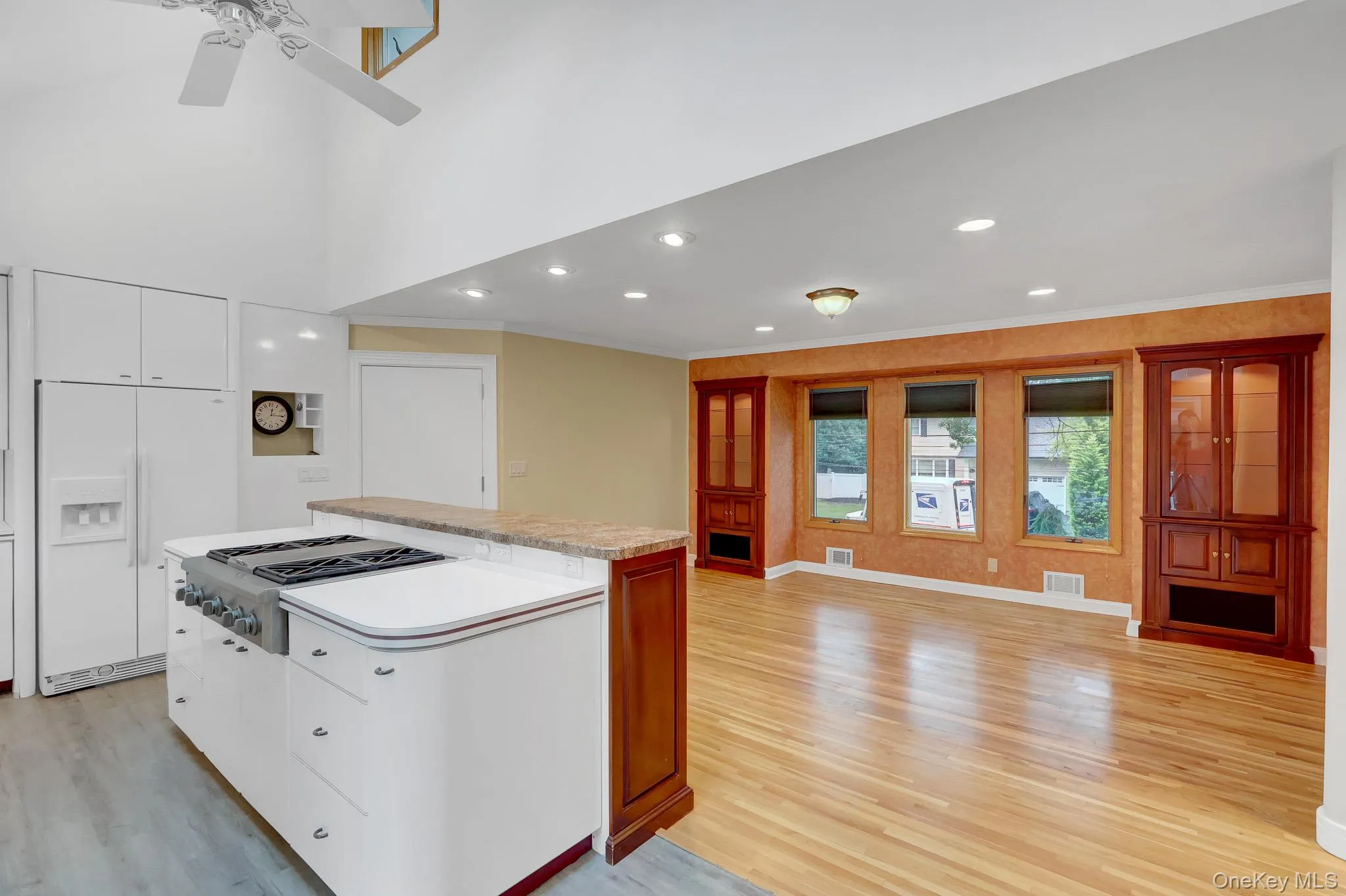 Kitchen island with a built-in range and a breakfast bar, white cabinetry, vaulted ceiling, recessed lighting, and wood-finish flooring Kitchen island with a built-in range and a breakfast bar, white cabinetry, vaulted ceiling, recessed lighting, and wood-finish flooring