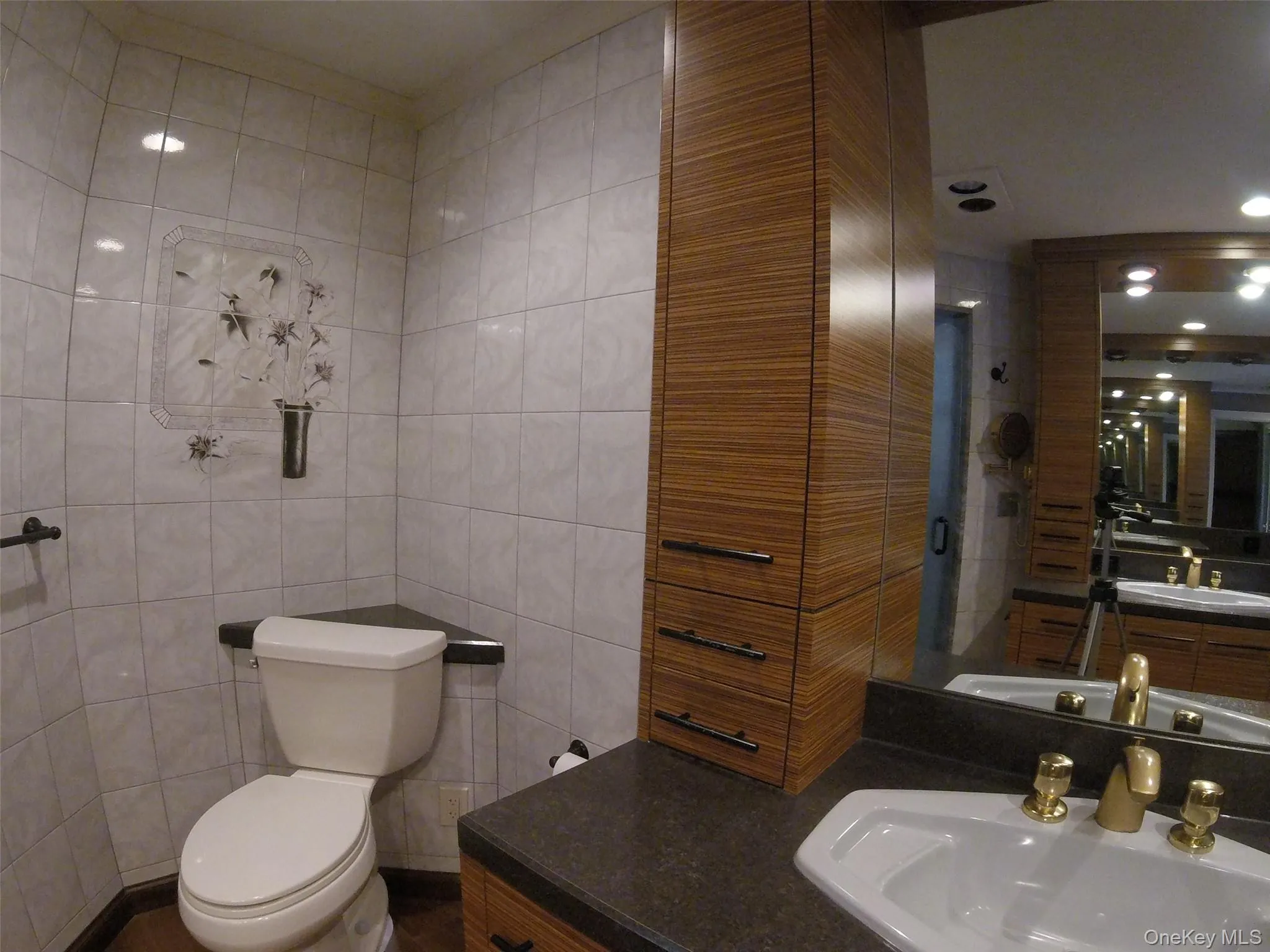 Bathroom featuring wood-finish cabinetry, a large vanity mirror, and a white corner toilet Bathroom featuring wood-finish cabinetry, a large vanity mirror, and a white corner toilet