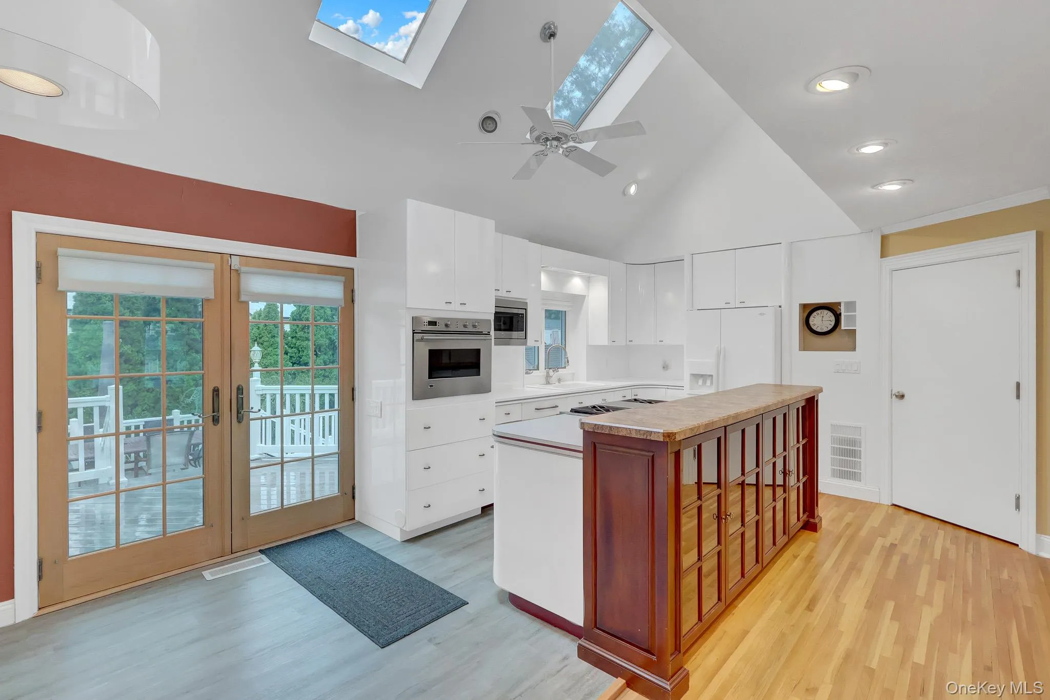 Vaulted ceiling with multiple skylights, integrated kitchen appliances, white cabinetry, wood-finish flooring, and direct access to an outdoor deck Vaulted ceiling with multiple skylights, integrated kitchen appliances, white cabinetry, wood-finish flooring, and direct access to an outdoor deck