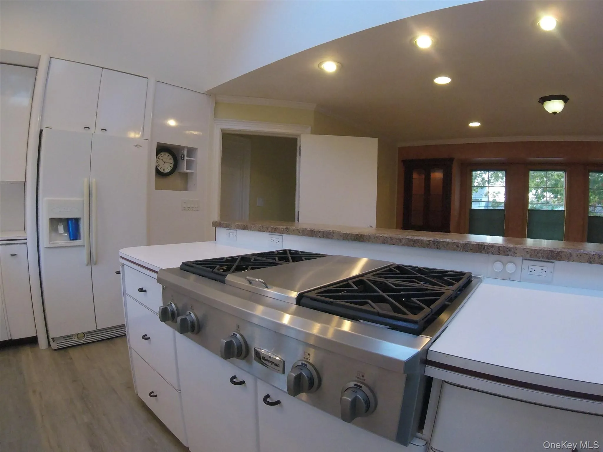 Kitchen featuring a stainless steel gas range, white cabinetry, light wood-finish flooring, recessed ceiling lighting, and a breakfast bar with a stone-look countertop Kitchen featuring a stainless steel gas range, white cabinetry, light wood-finish flooring, recessed ceiling lighting, and a breakfast bar with a stone-look countertop