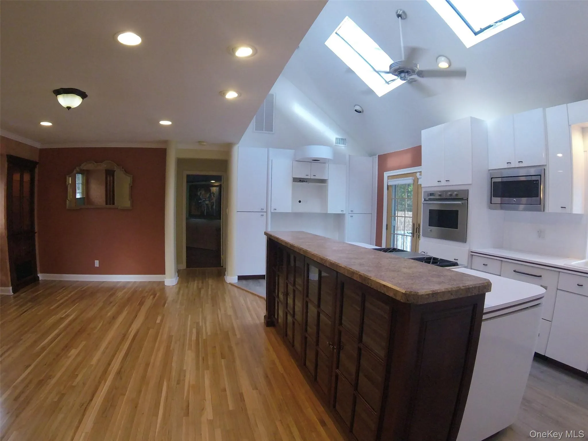 Kitchen and dining area featuring skylights, recessed lighting, wood-finish flooring, a vaulted ceiling, and white cabinetry Kitchen and dining area featuring skylights, recessed lighting, wood-finish flooring, a vaulted ceiling, and white cabinetry