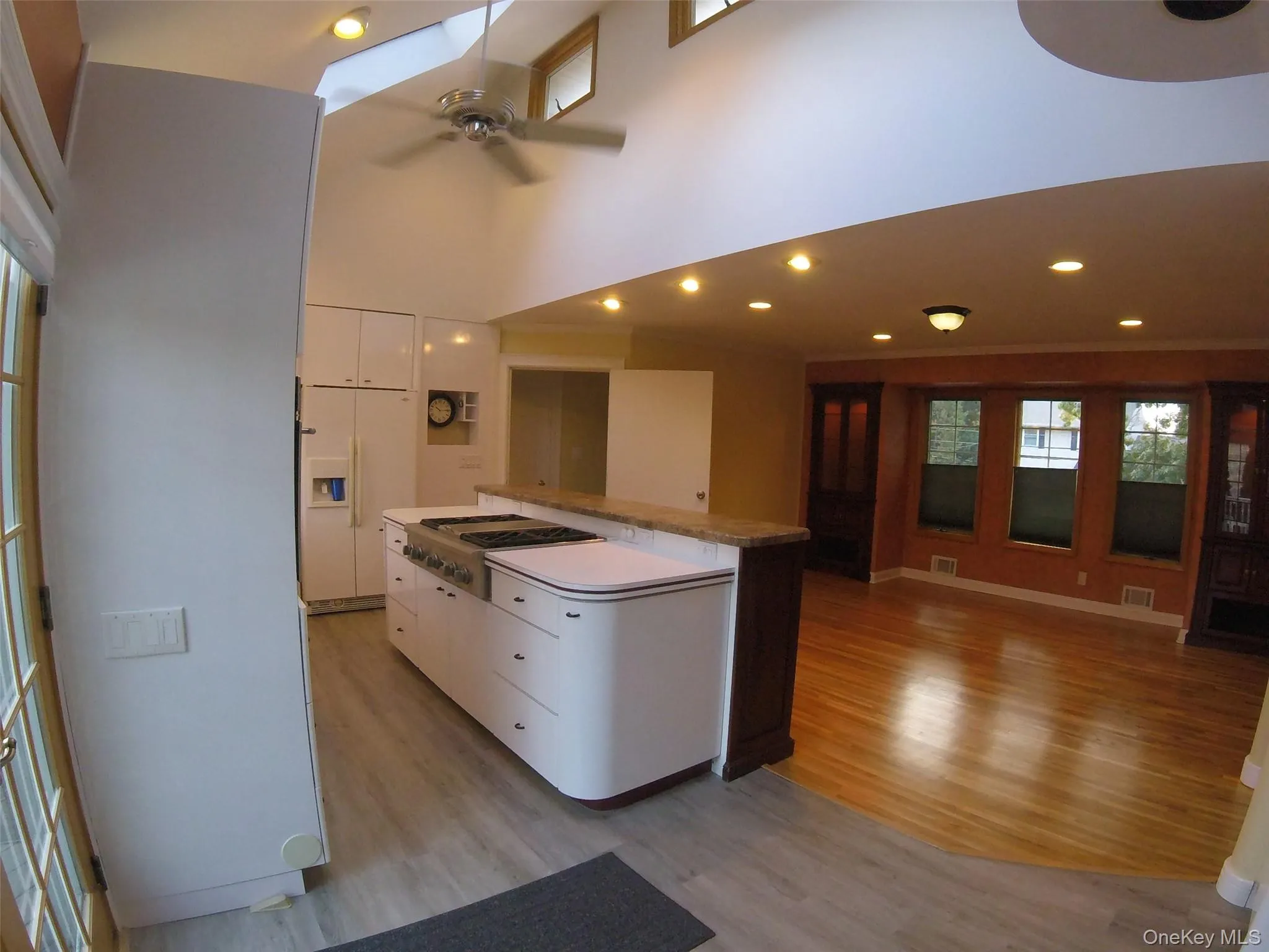 Kitchen featuring white cabinetry, a center island with a built-in range, a light-colored countertop, and wood-finish flooring Kitchen featuring white cabinetry, a center island with a built-in range, a light-colored countertop, and wood-finish flooring