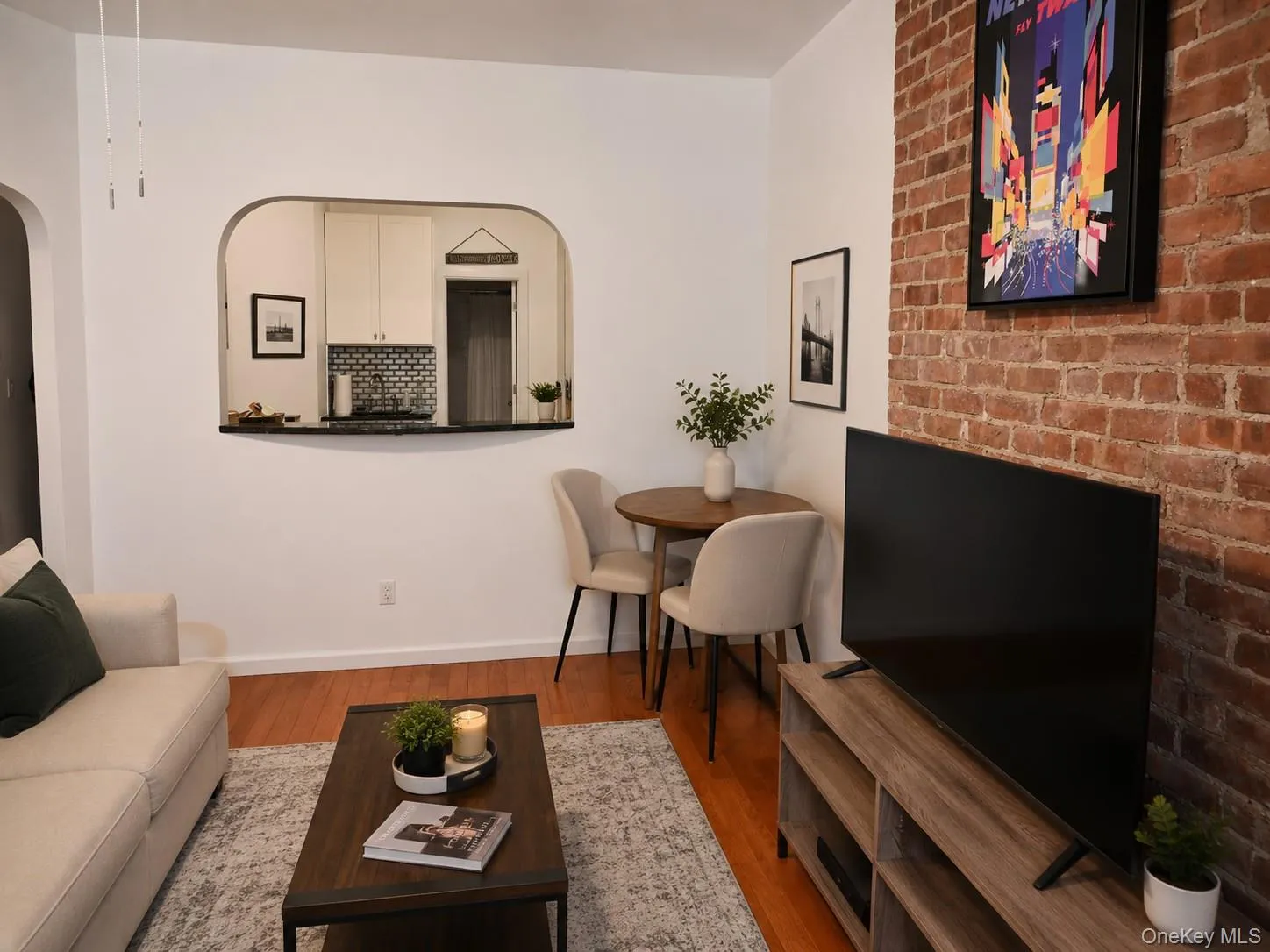 Exposed brick accent wall, wood-finish flooring, and a kitchen pass-through with a dark countertop (virtually staged) Exposed brick accent wall, wood-finish flooring, and a kitchen pass-through with a dark countertop (virtually staged)
